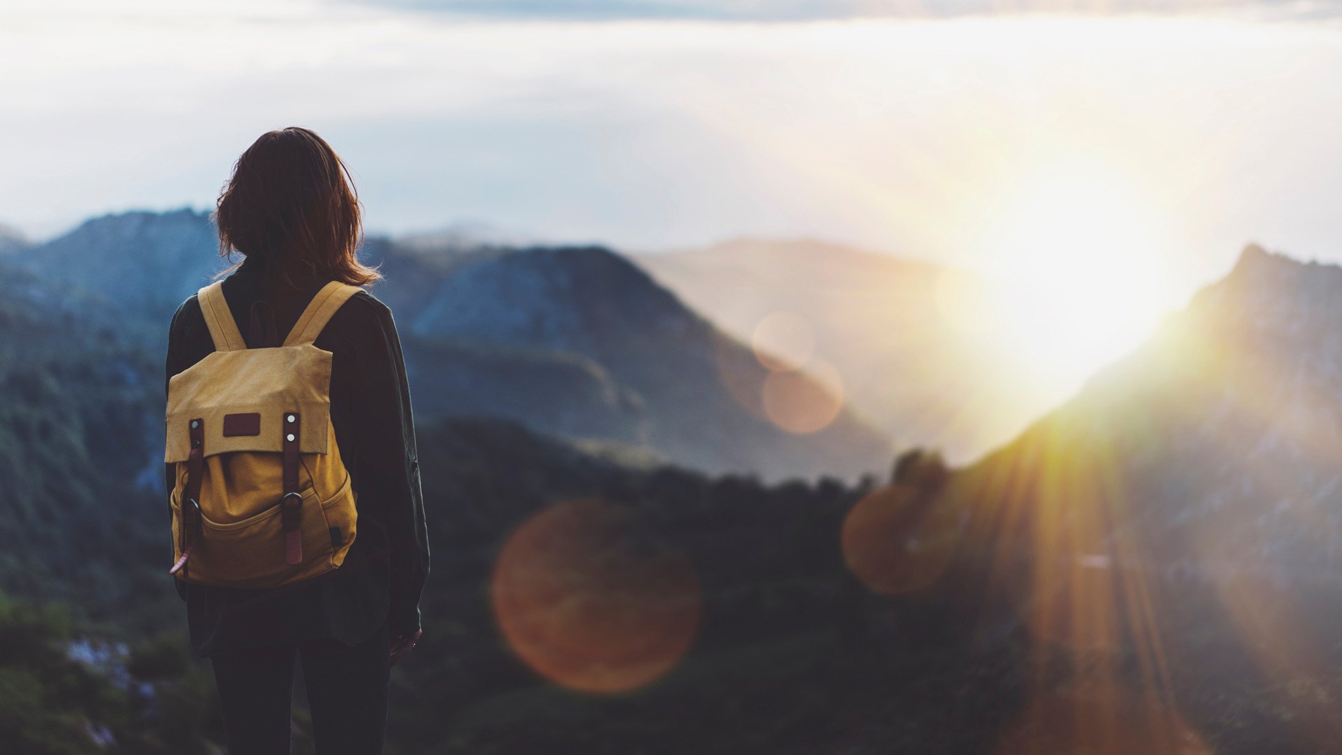 Woman with a yellow backpack gazing at misty Mt. Hood mountain views on a cloudy day near RAVN HAUS modern alpine vacation rental in Government Camp, Oregon.