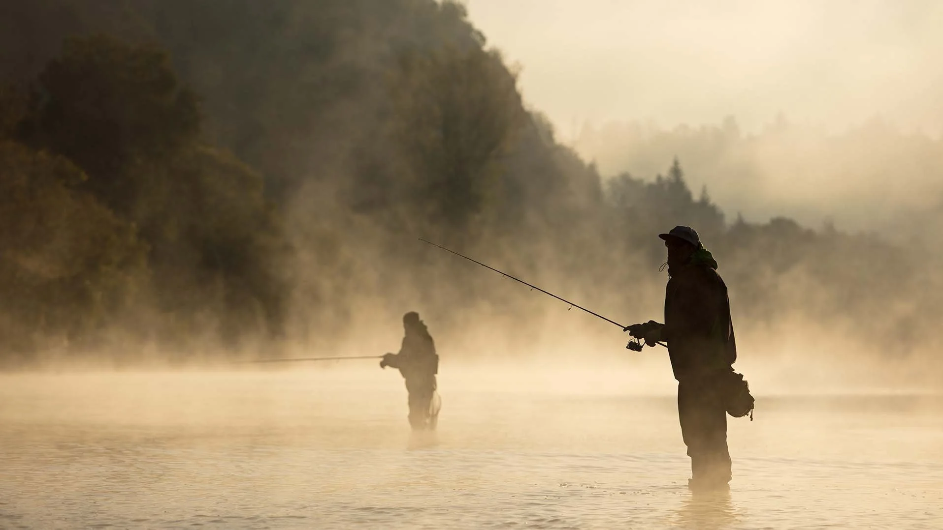 Two anglers fly fishing in misty morning light on a Mt. Hood river near RAVN HAUS modern alpine vacation rental in Government Camp, Oregon.