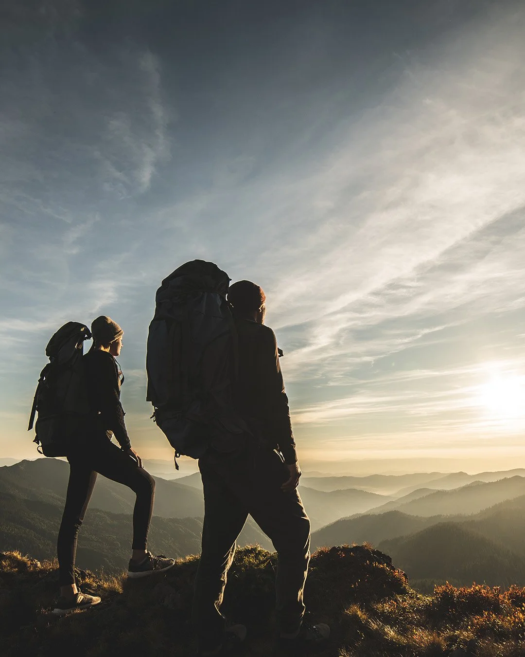 Two backpackers silhouetted against a golden sunset sky on a Mt. Hood trail near RAVN HAUS modern alpine vacation rental in Government Camp, Oregon, perfect for hiking and snowshoeing adventures.
