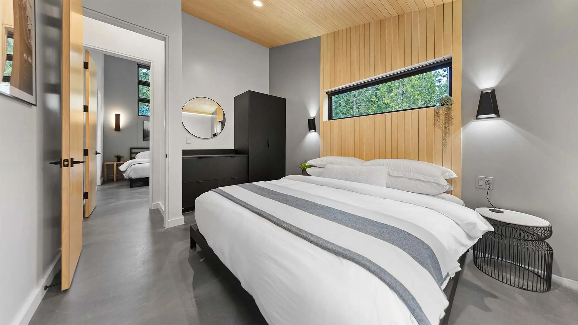 Alpine King room at RAVN HAUS Mt. Hood vacation rental with king bed, wood slat headboard wall, horizontal window to the trees, and black wardrobe.