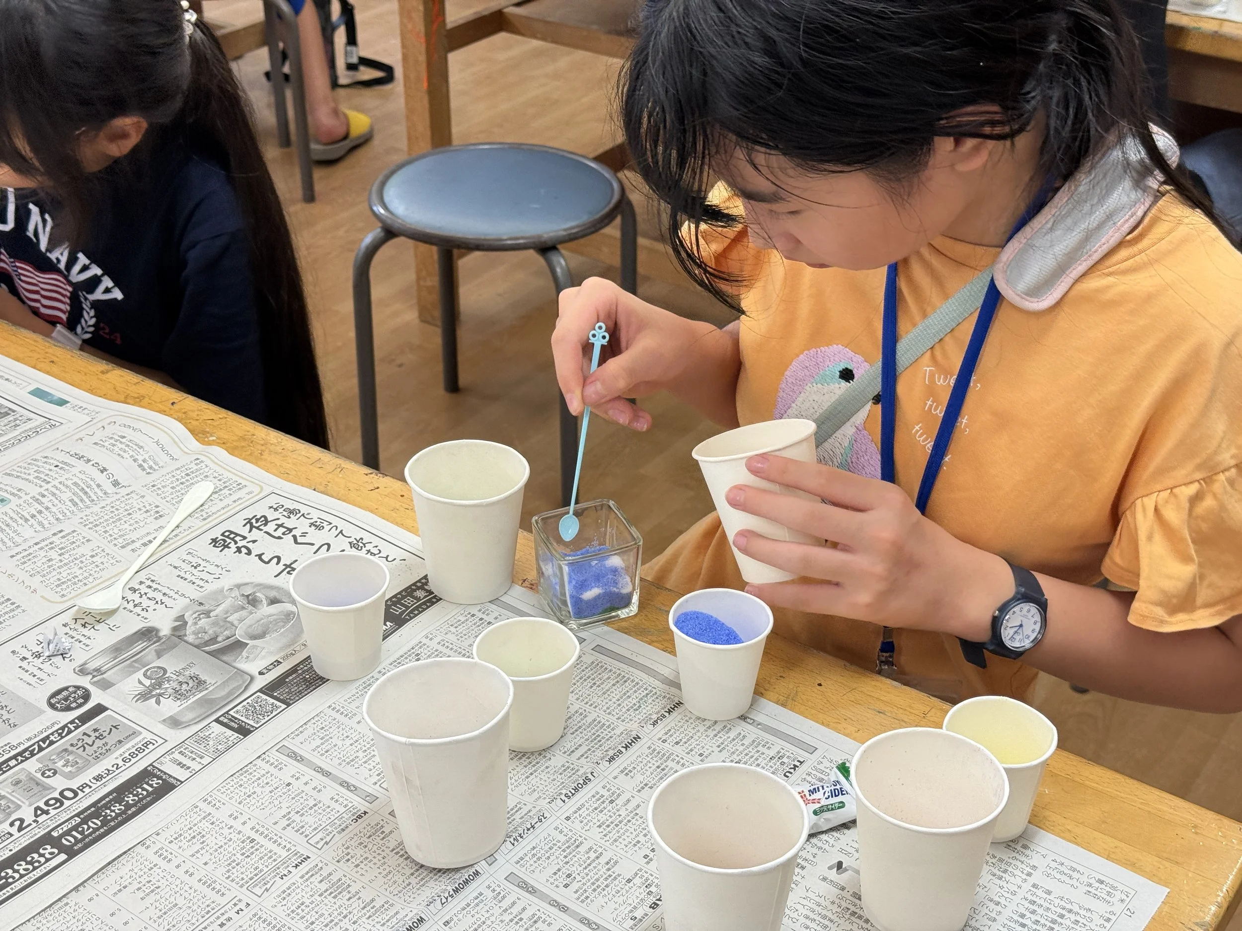 子供たちがクラフト用のアイスクリームカップにビーズを入れている様子。