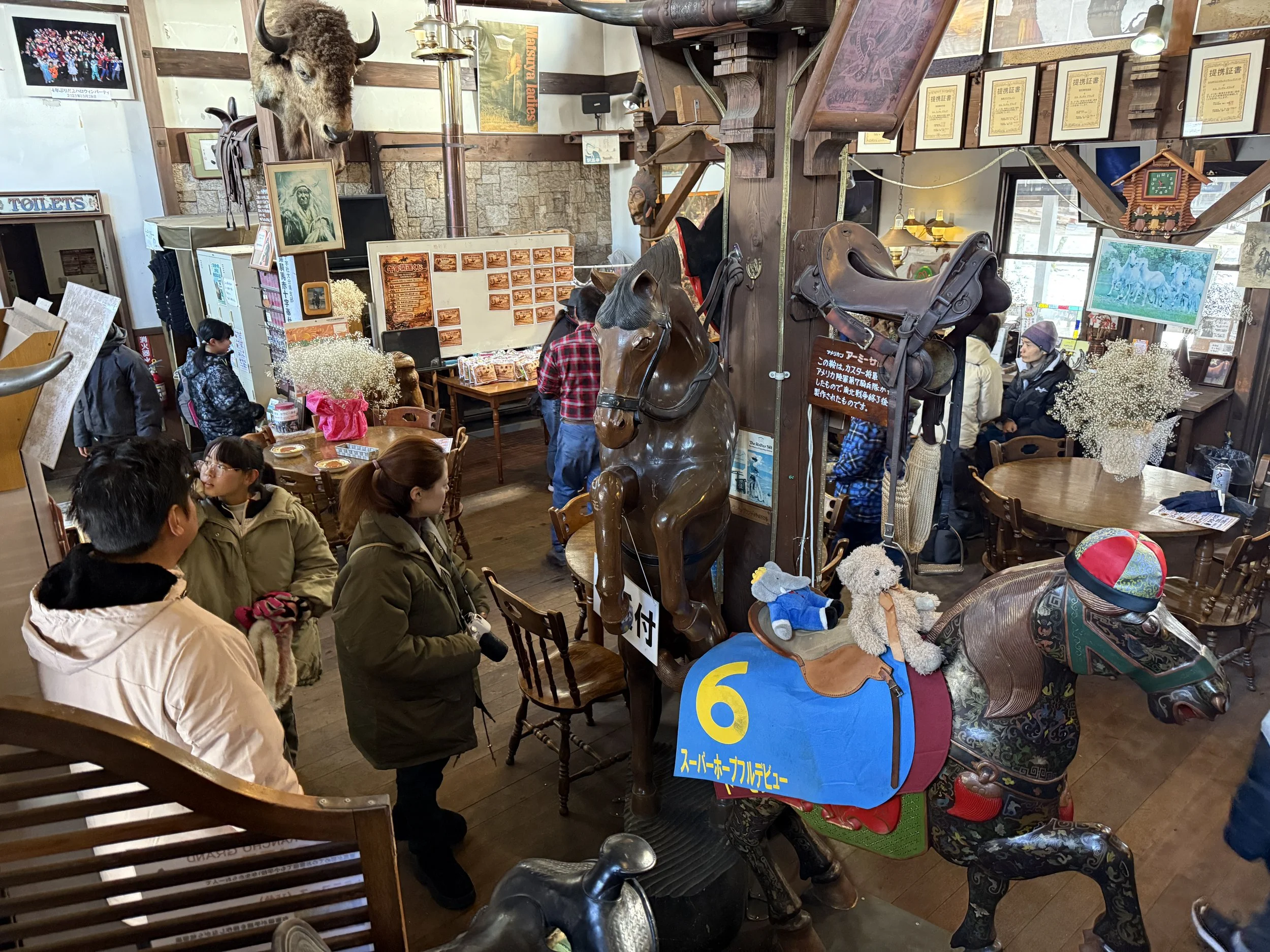 店内には馬の置物やぬいぐるみ、木製の馬の乗り物が飾られている。多くの人が店を訪れている。