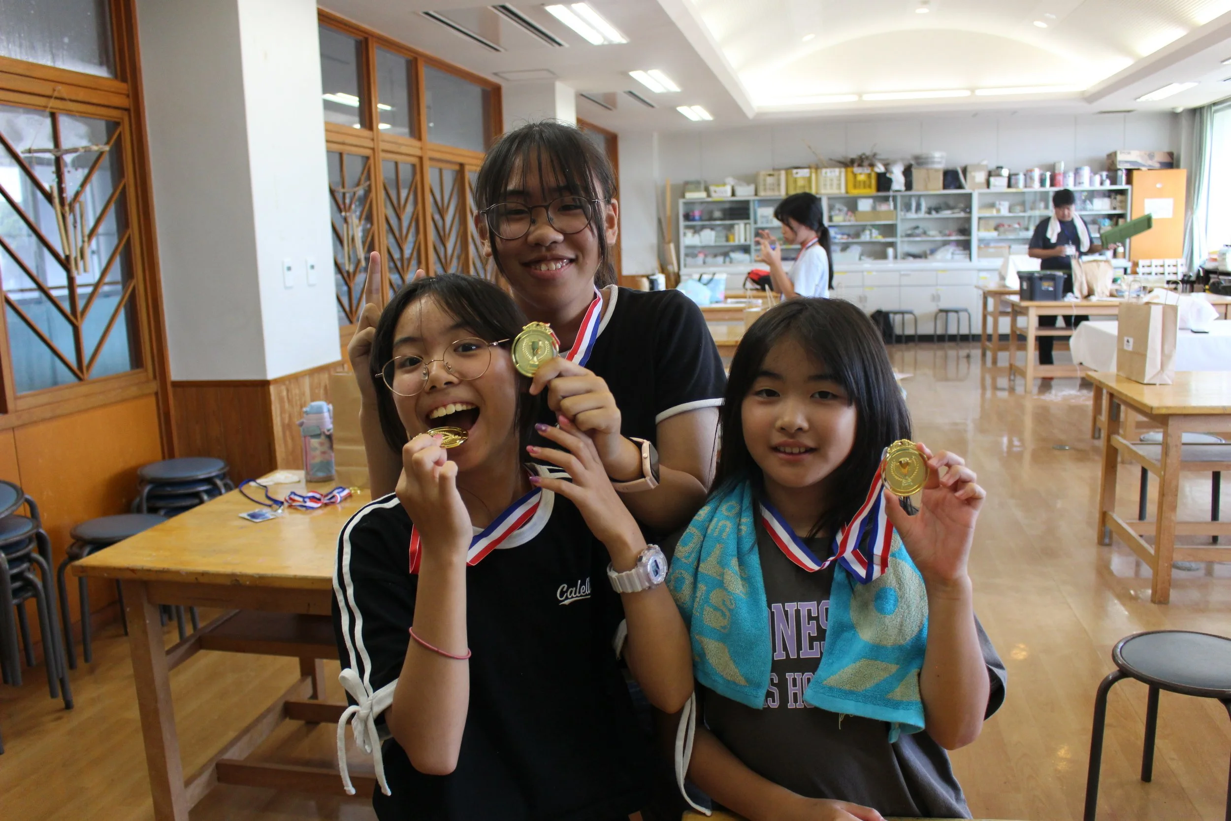 メダルを持つ3人の少女たち、屋内の部屋で笑顔で写真を撮っている