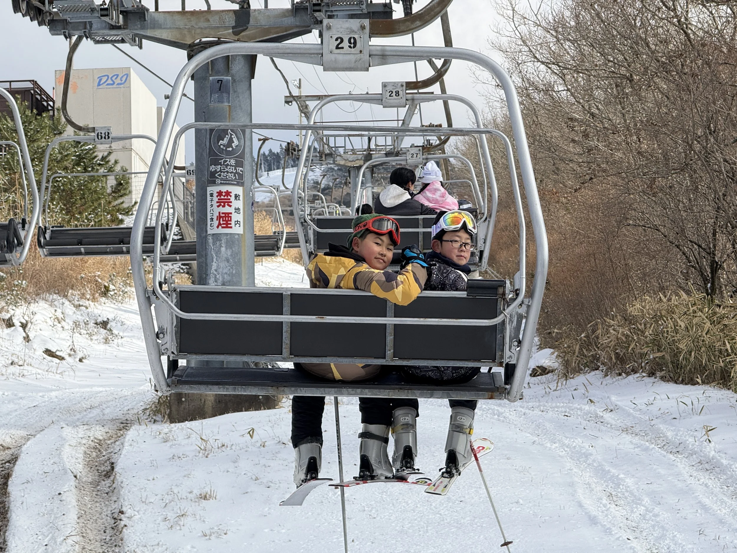 スキーリフトに乗る子供たちのグループ。雪山と木々の後ろに座っている子供たちとスキー板。