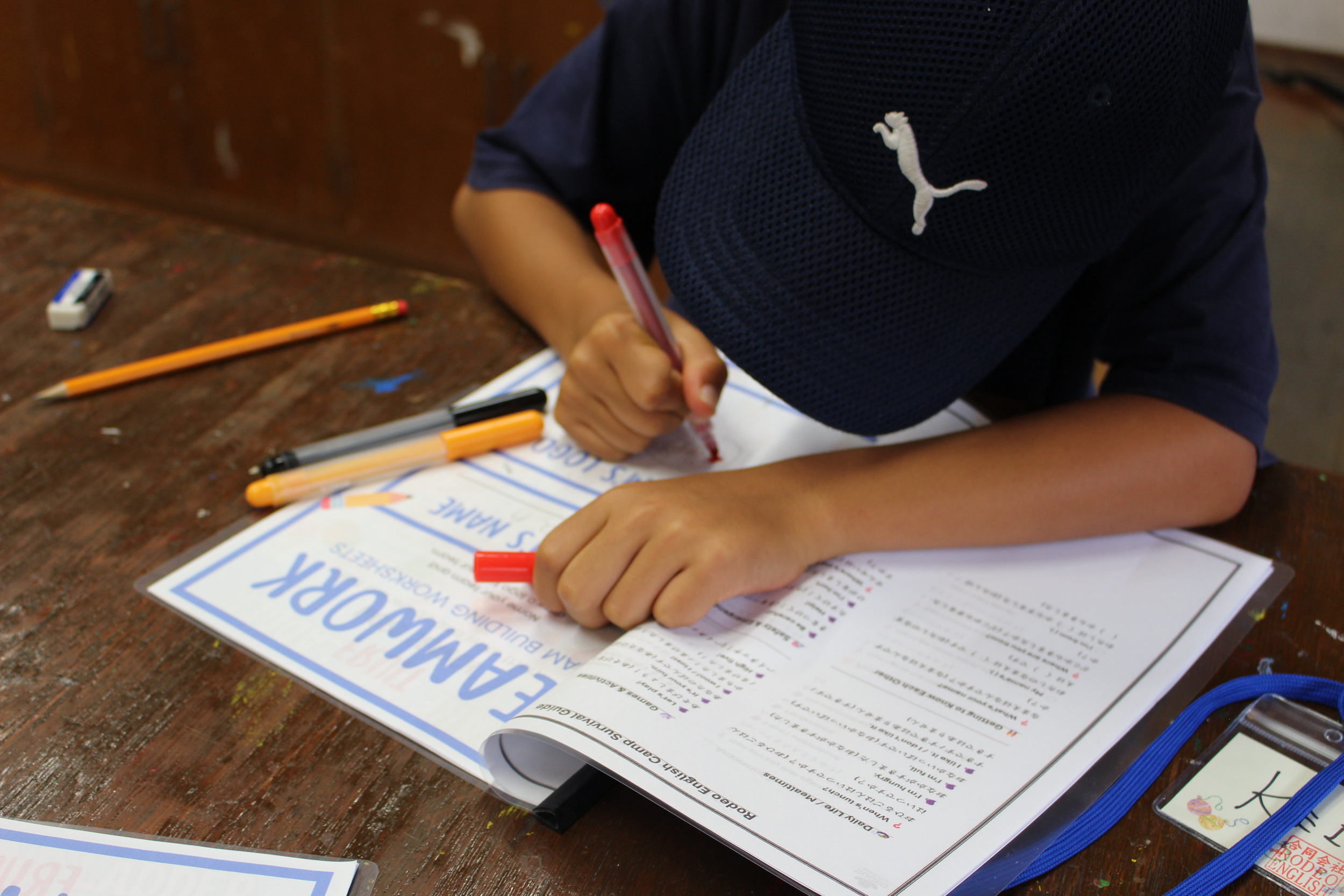 子供が学校の課題に取り組んでいる様子。机の上に教科書やペンが置かれている。