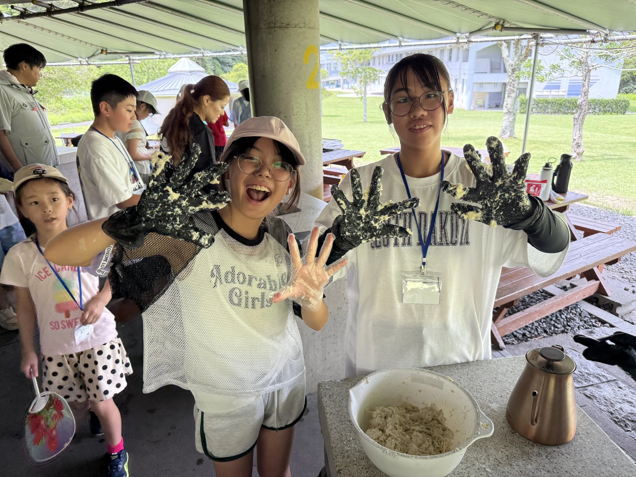 屋外のバーベキュー場で、子供と大人がパンをこねる活動をしています。二人は手に粉をつけて笑顔でポーズをとっています。