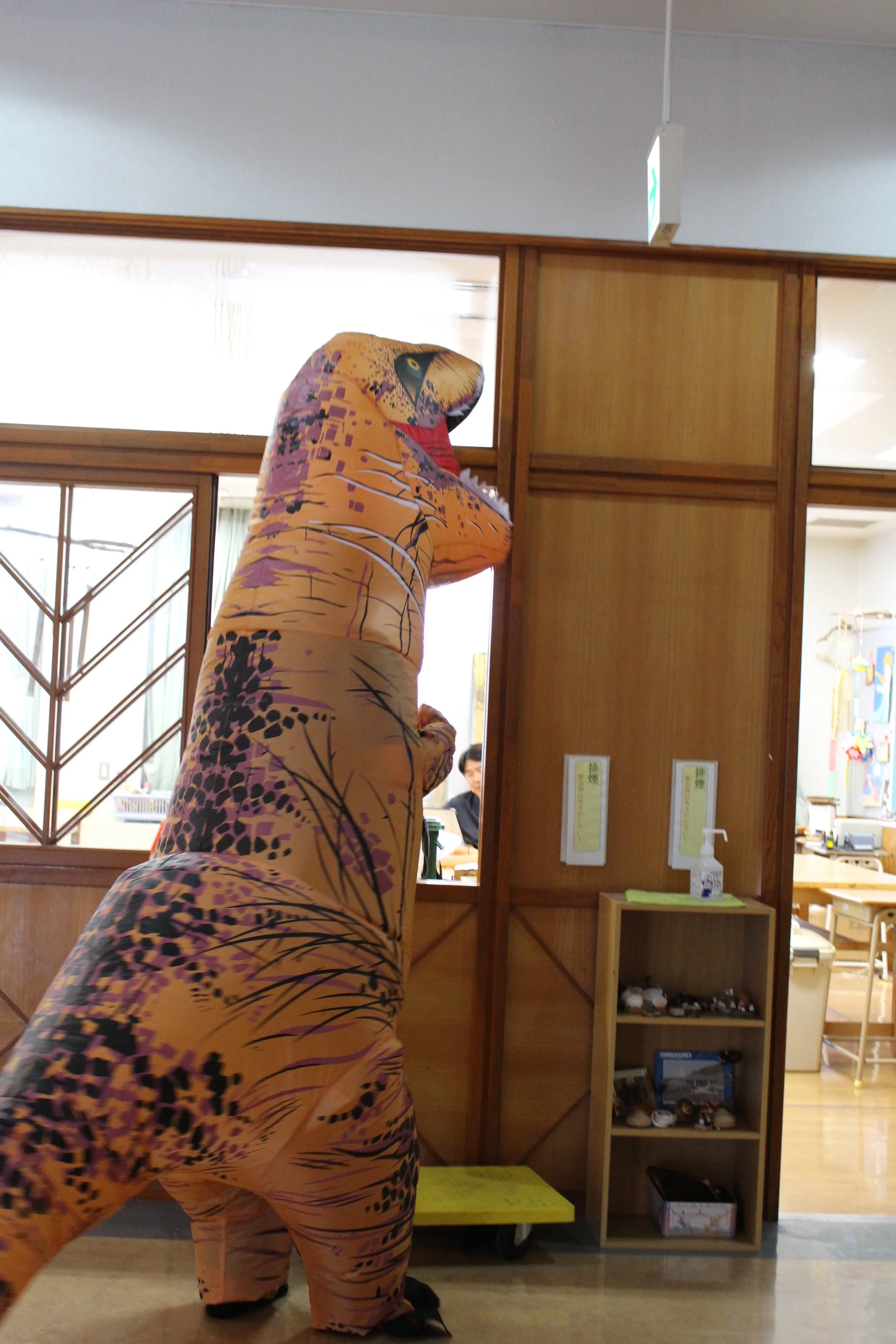 恐竜の着ぐるみを着た人が建物の中に入ろうとしている