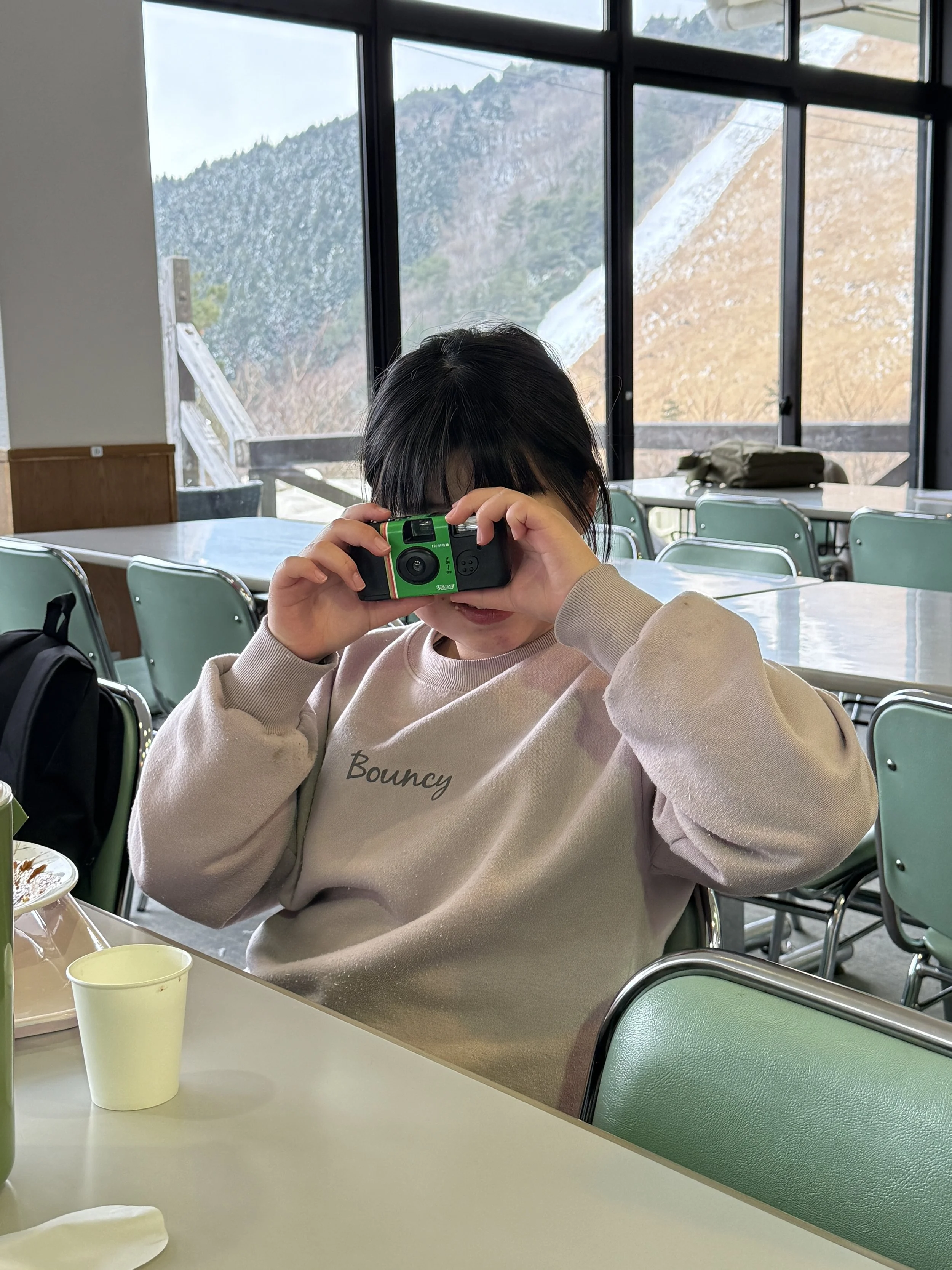 窓の外に山が見える室内のレストランで、子供がカメラを持っている写真