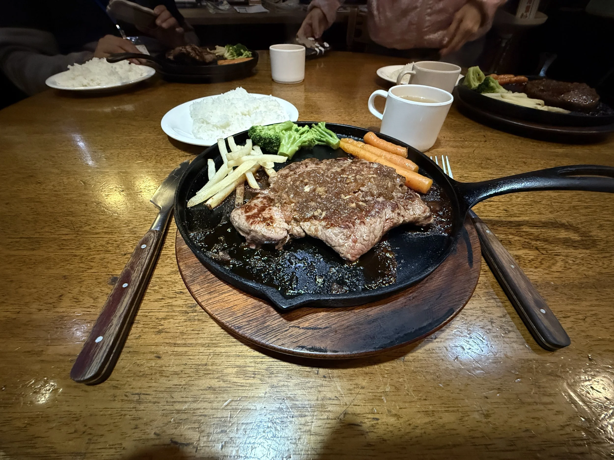 ステーキがついた熱々の鉄板料理と、添えられた野菜やにんじんの写真。