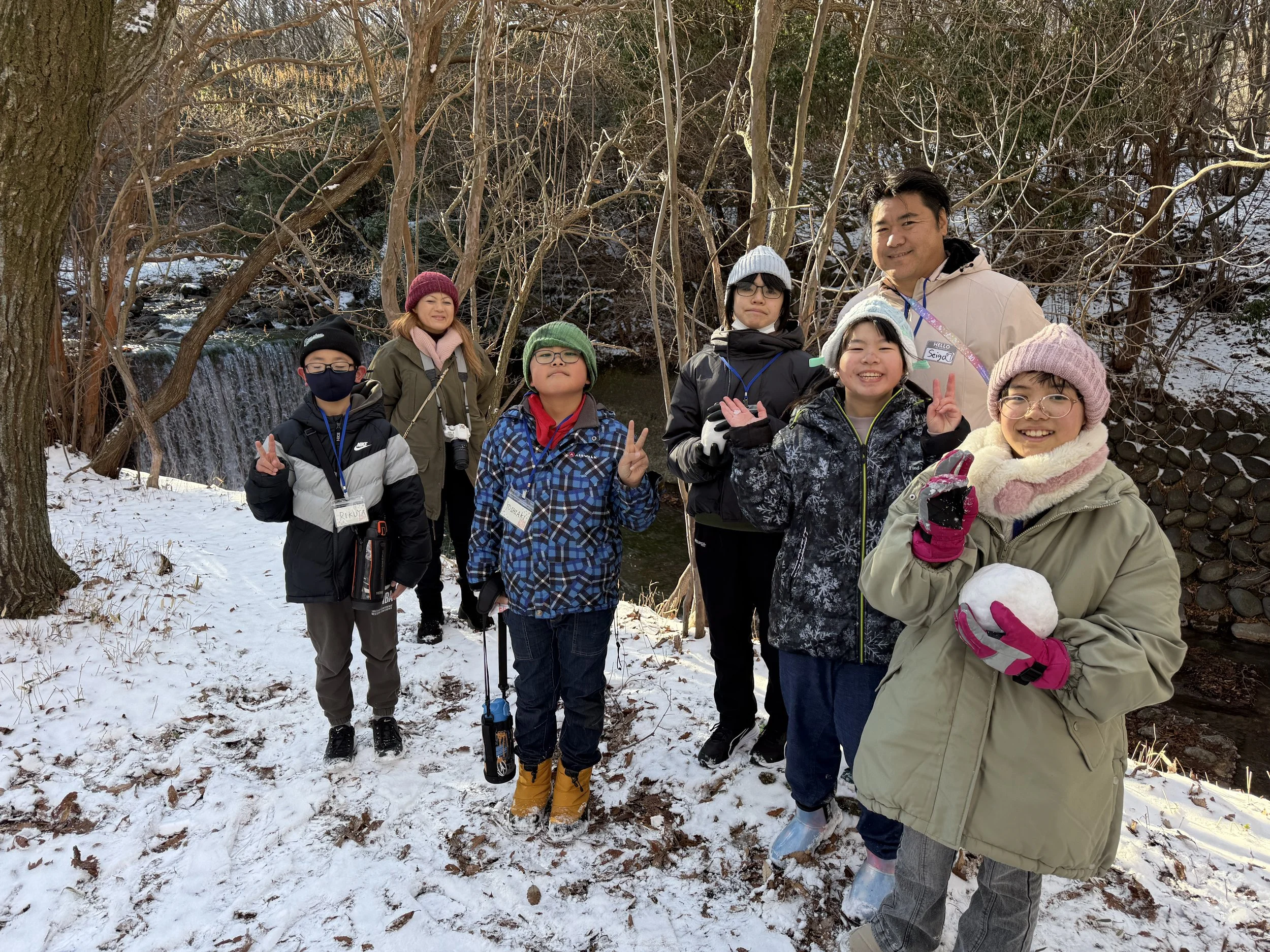 雪の中、川のほとりでグループの子供と大人が写真を撮っている。