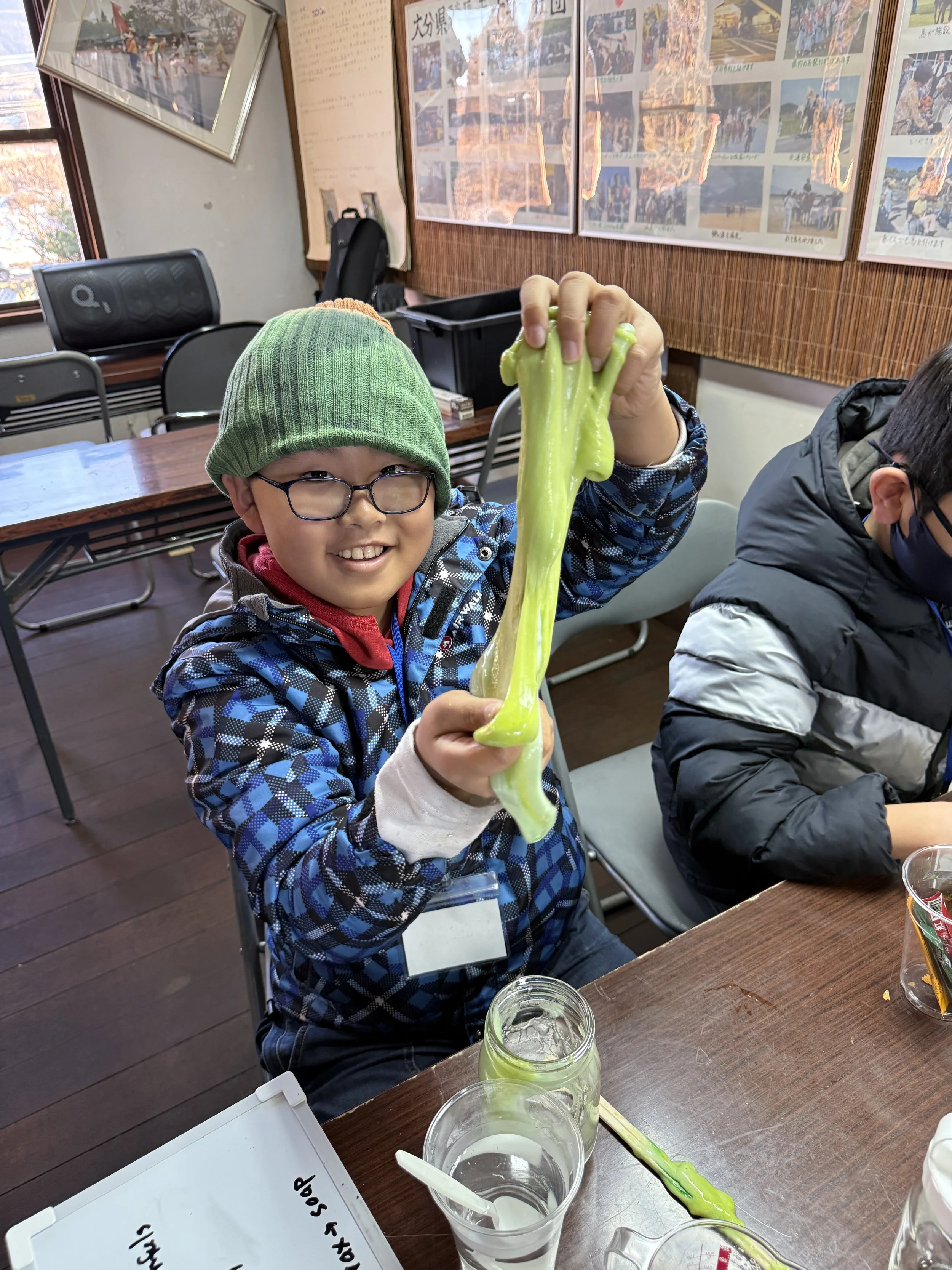 緑色の粘土を持つ少年と、その横にある粘土と水の入ったグラス