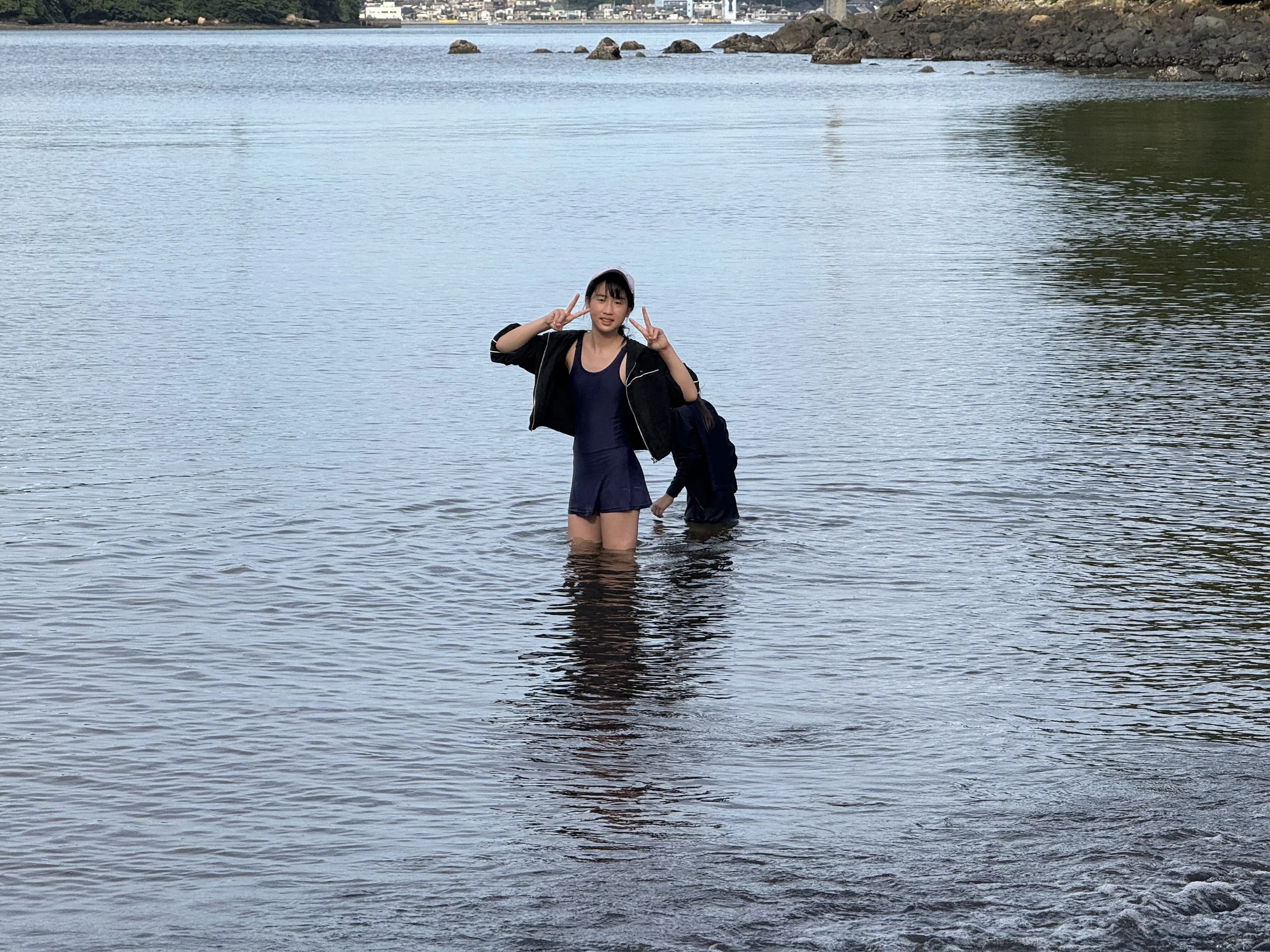 女性と子供が川の中に立っている。女性は笑顔でピースサインをしている。
