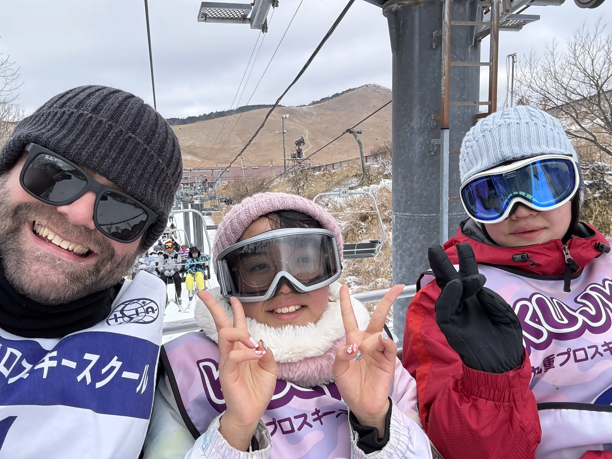 スキーやスノーボードをしている人々がリフトに乗っている冬山の風景。３人の子供と大人が笑顔でポーズをとっている。