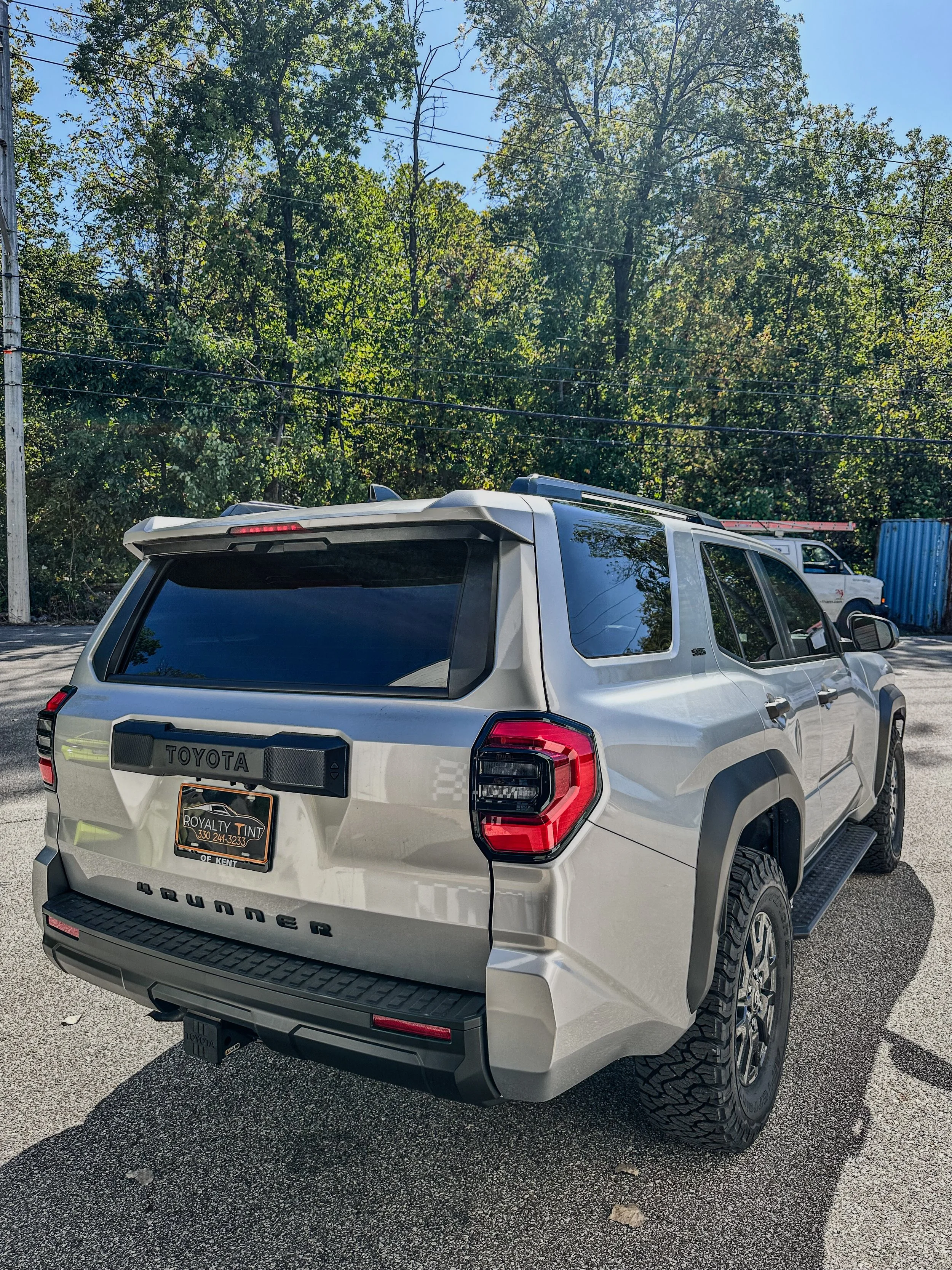 Rear view of a white Toyota Tundra SUV parked on a paved lot, with trees and a blue sky in the background.