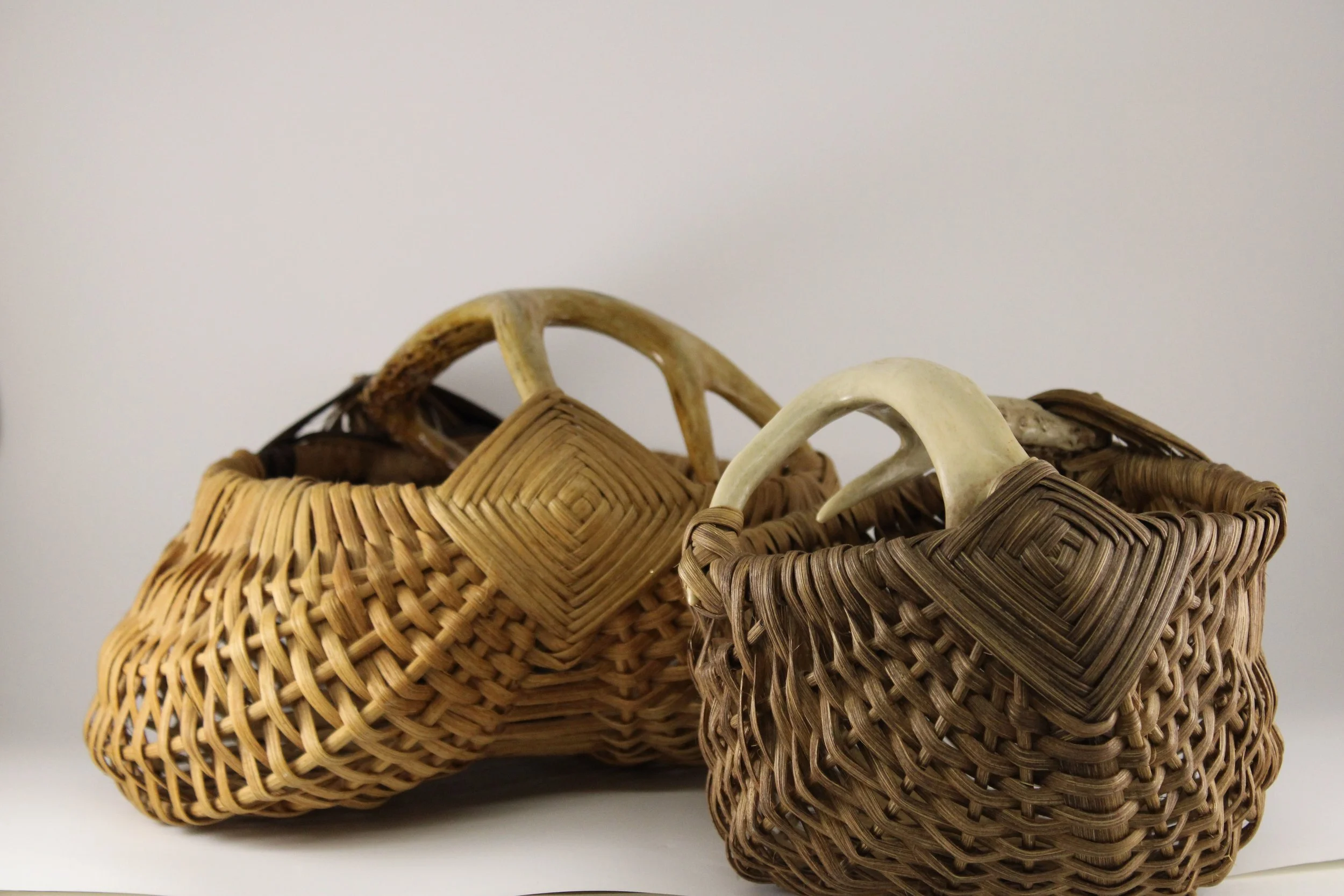 Three woven baskets with handles, placed on a white surface against a white background.