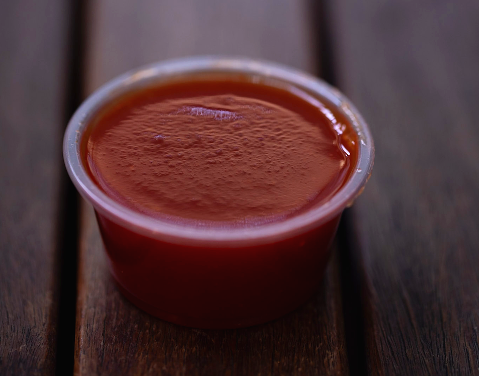 A small cup of sauce on wooden surface.