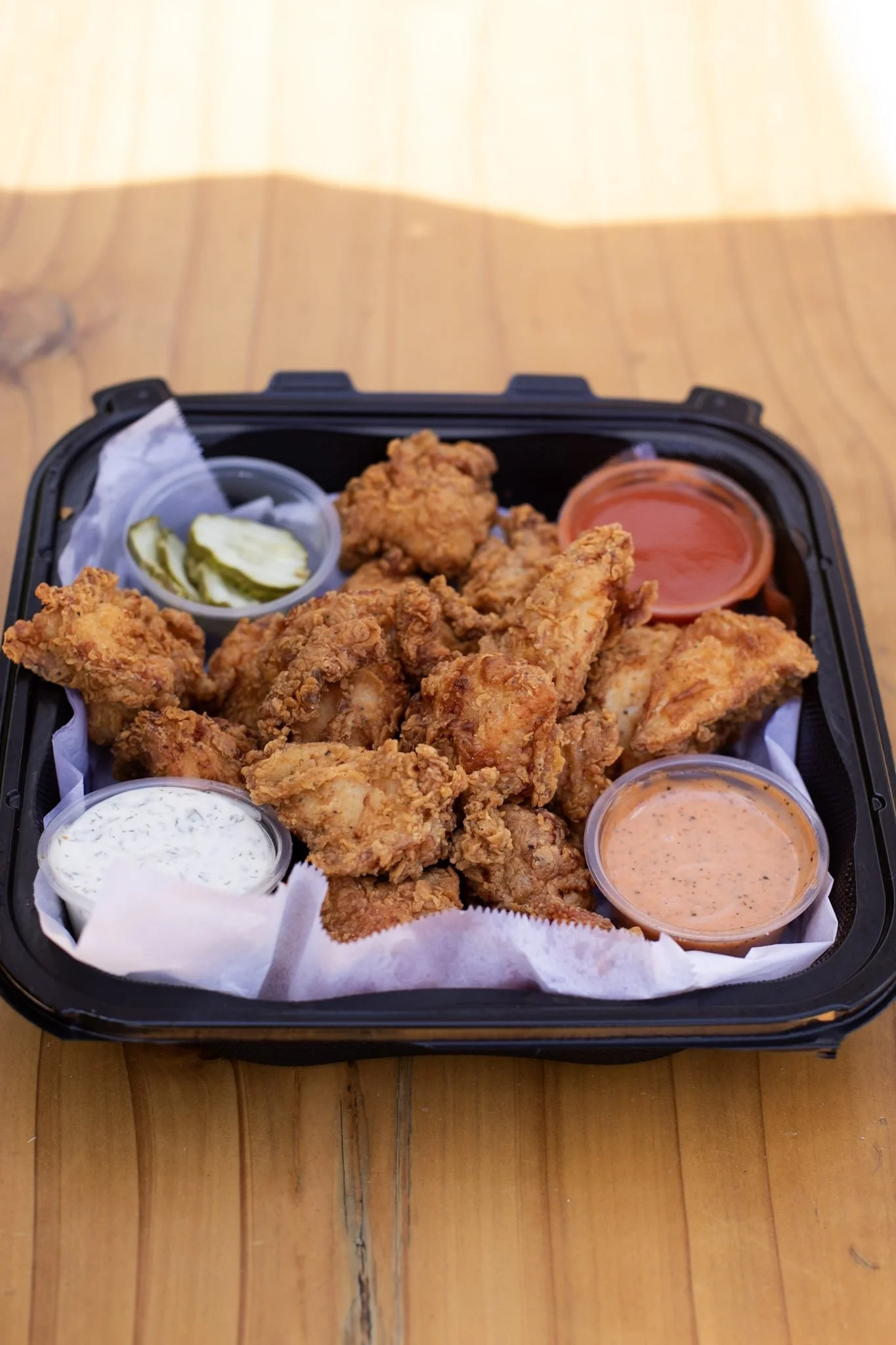 Chicken nuggets, pickles, ramequins with sauce on a black tray with parchment paper.