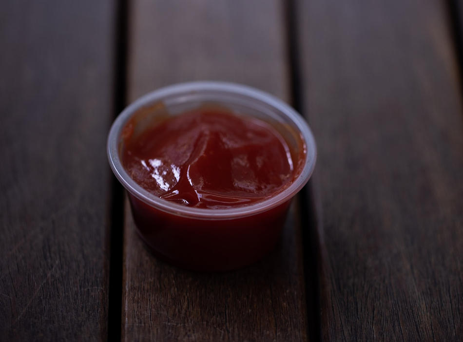 A small clear cup of scorpion sauce placed on a wooden surface.