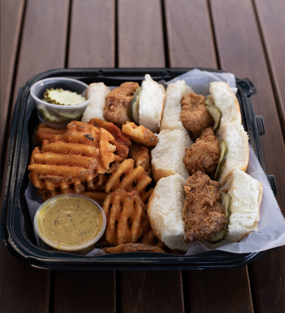 A plate of nuggtown sliders with waffle fries and two ramequins, one with pickles and one with sauce.