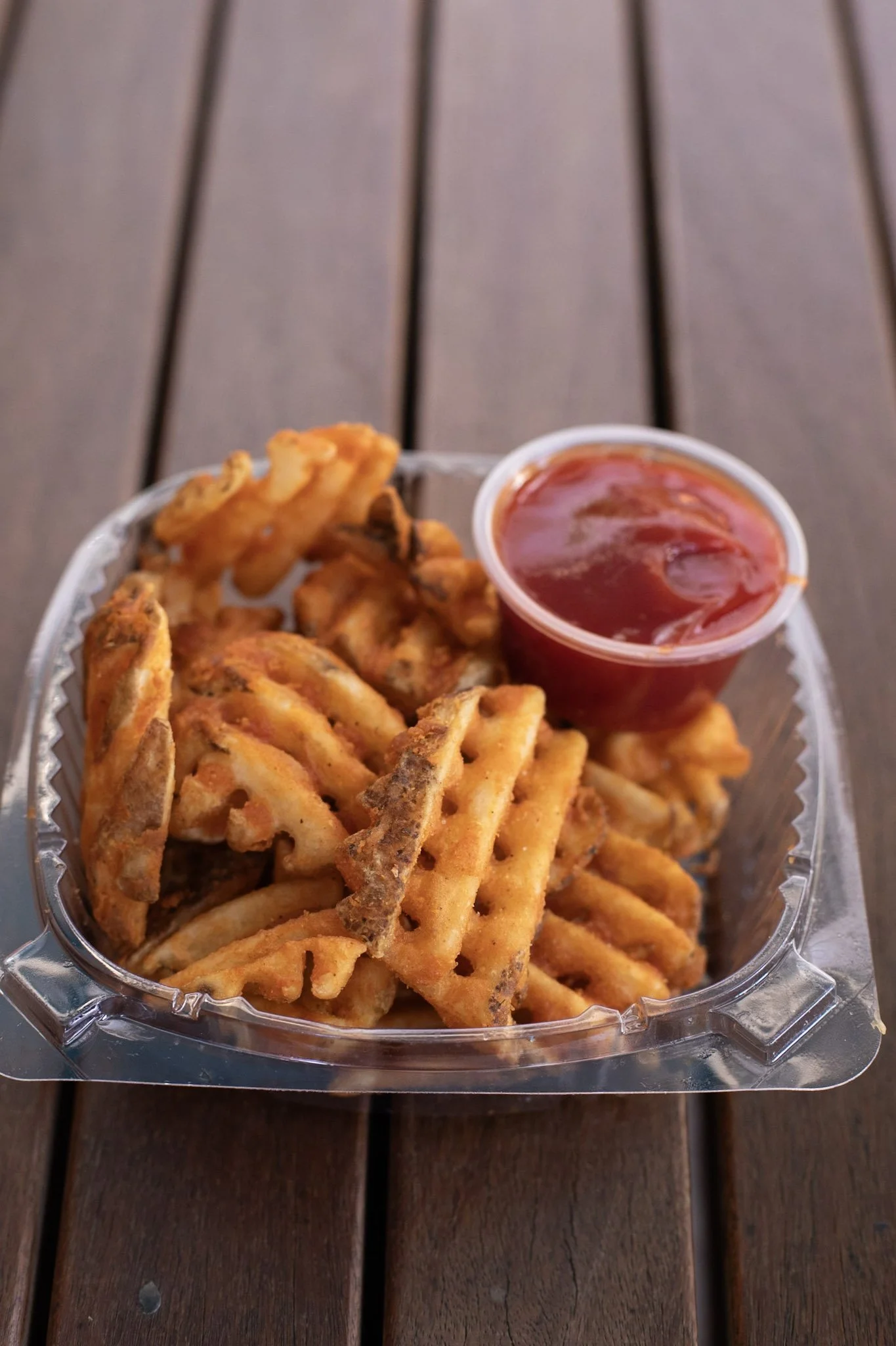 Waffle fries in a plastic tray with a ramequin filled with ketchup.