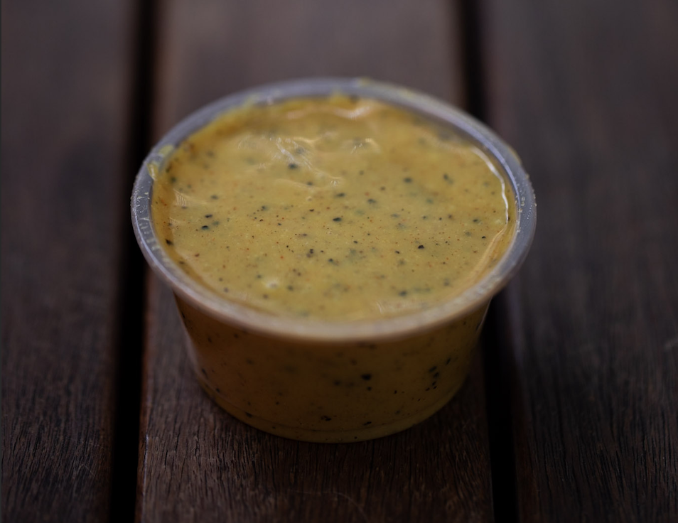 Container of honey mustard seeds in yellow mustard sauce on a dark wooden surface.