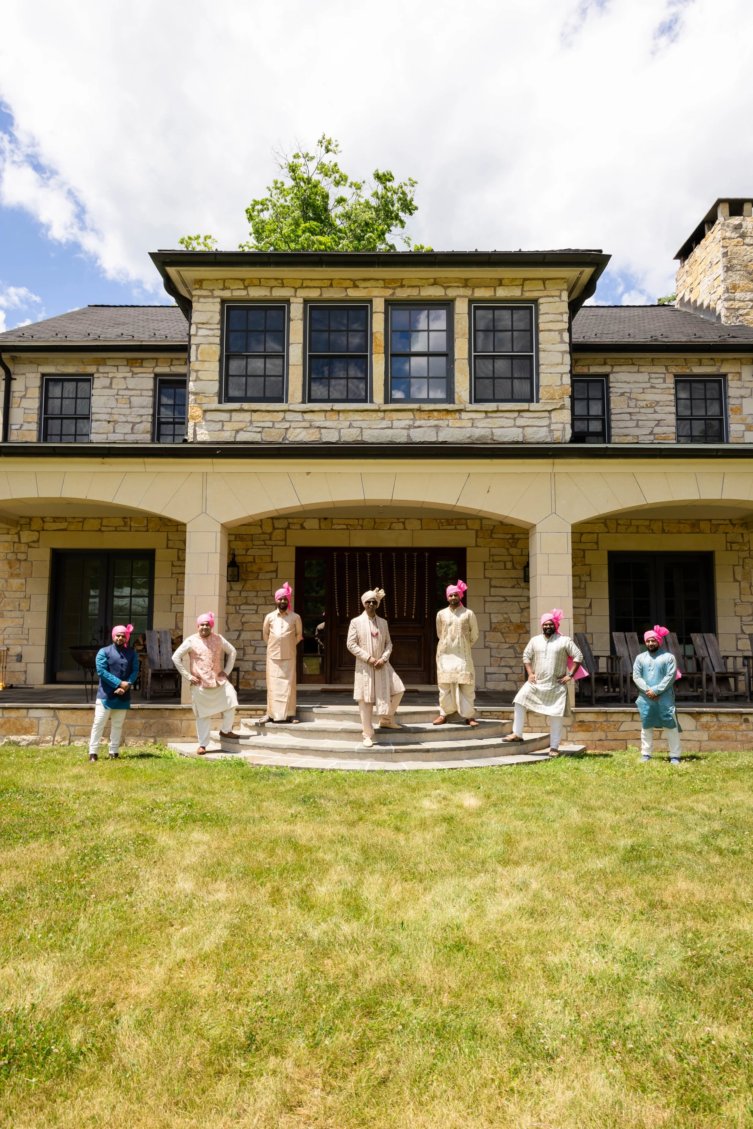 Group of men dressed in traditional Indian attire standing outside a stone house.