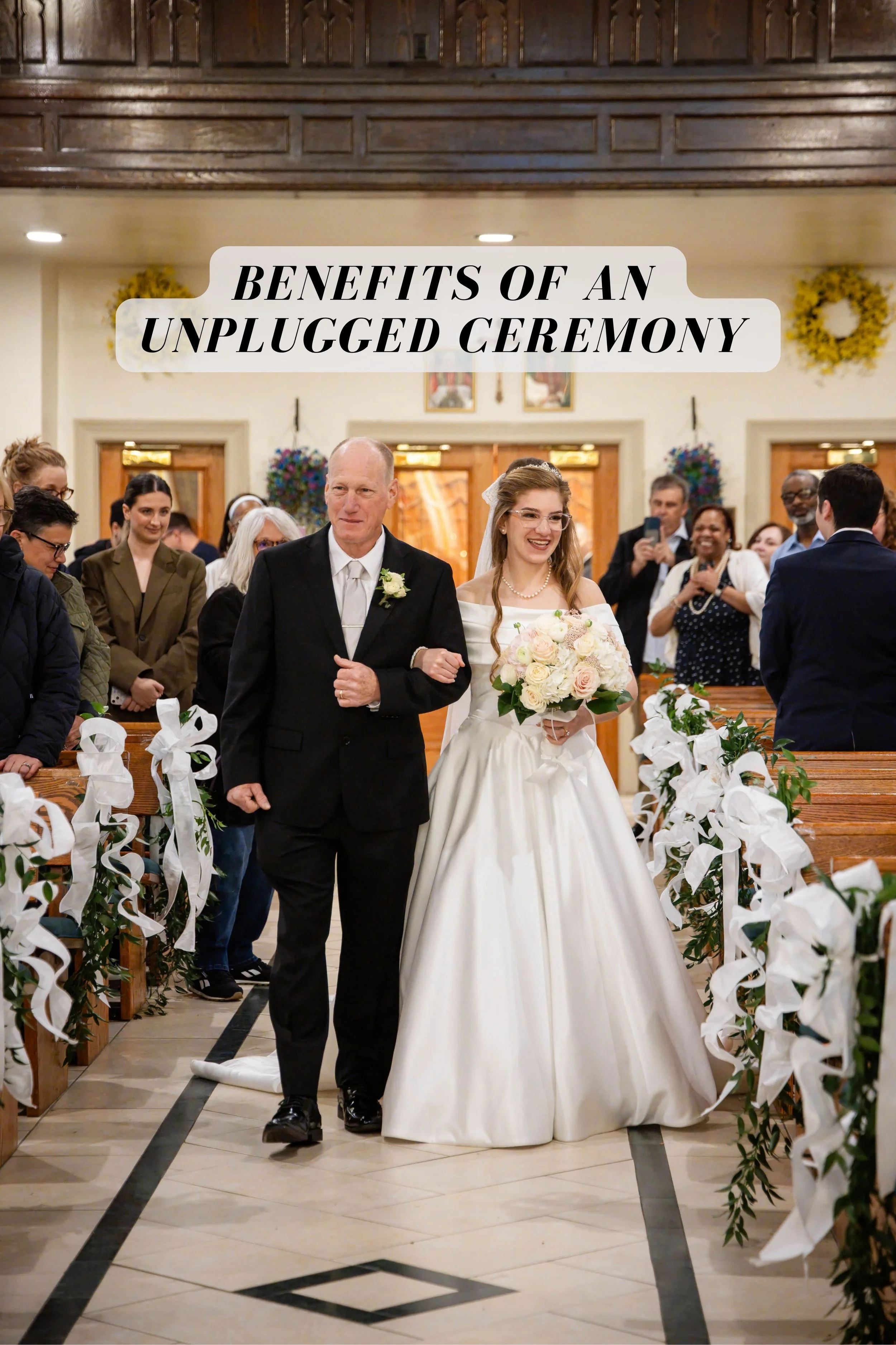 A bride, wearing a white wedding dress and holding a bouquet, walks down the aisle of a church accompanied by an older man in a black suit, likely her father. The church is decorated with white flowers and ribbons, and guests are smiling and taking photos.