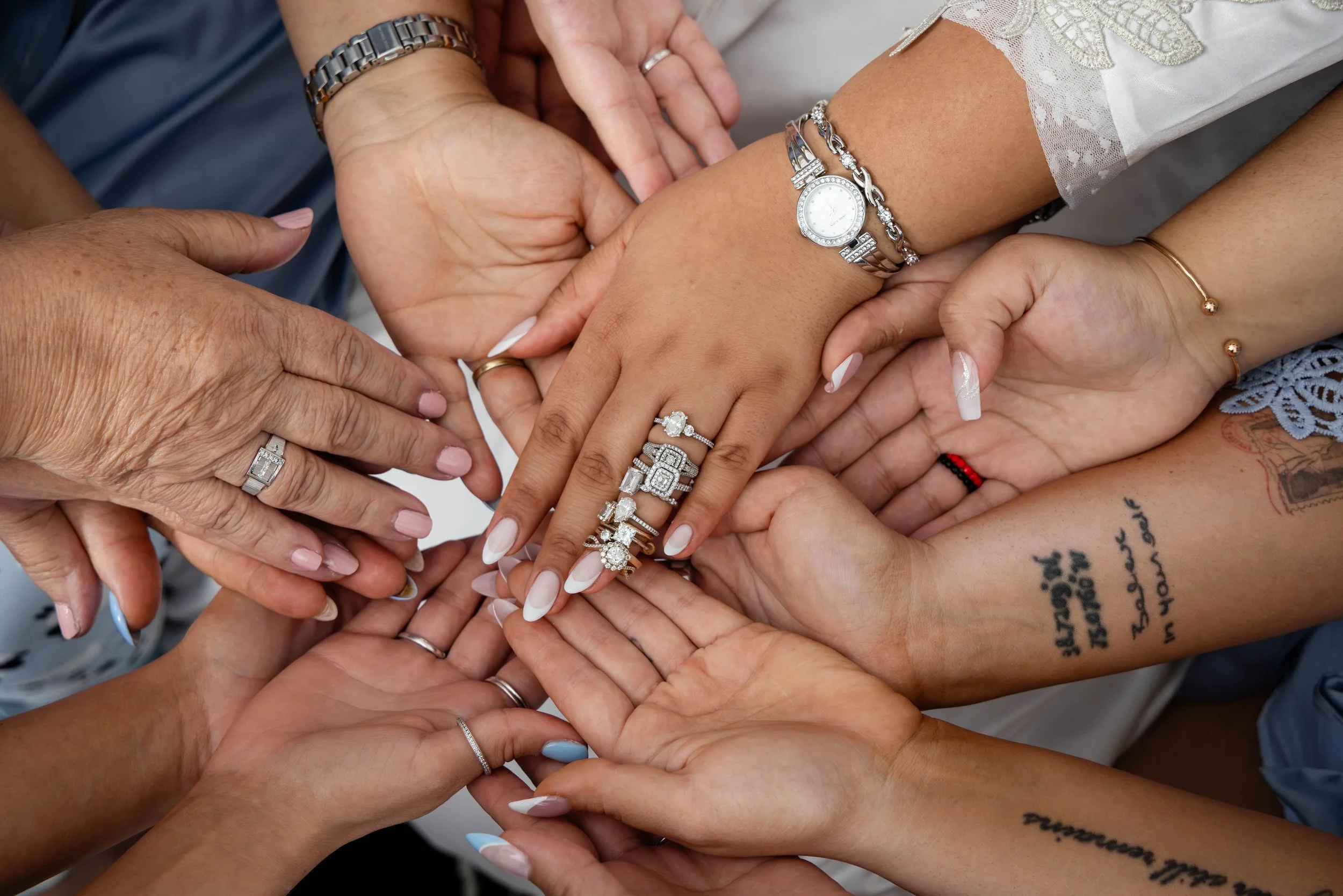 Multiple hands of diverse individuals stacked together, showing various rings, watches, and bracelets, symbolizing unity and celebration.