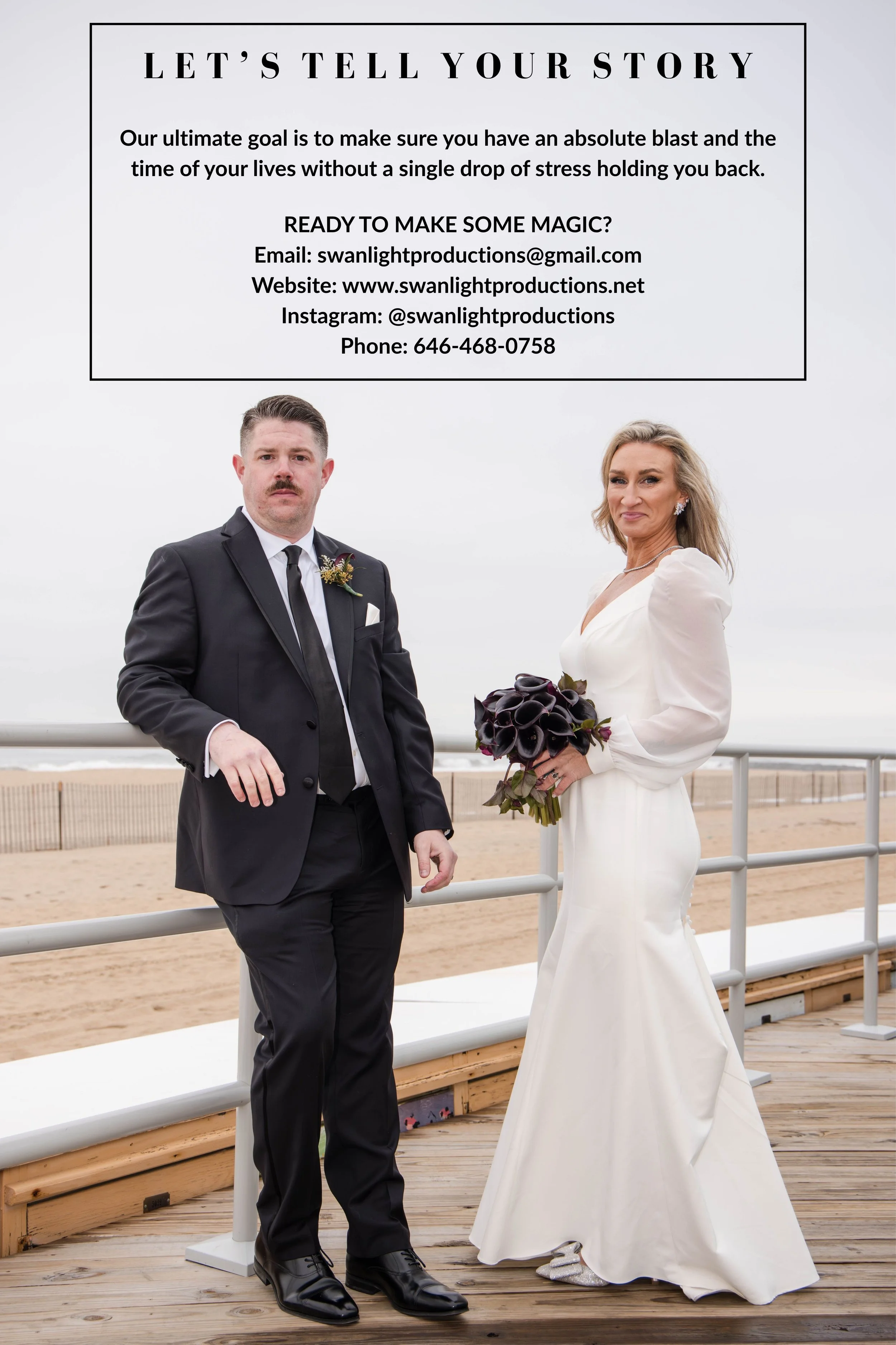 A man in a black suit and a woman in a white wedding dress standing on a wooden boardwalk at the beach, with a white railing and ocean in the background. The woman is holding a bouquet of dark purple calla lilies. Both are looking at the camera, and the woman has a slight smile.