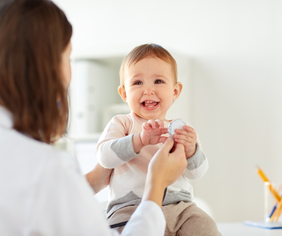 A young child with a happy expression holding a medicine syringe while sitting on a medical professional's lap, who is preparing to give a vaccination.