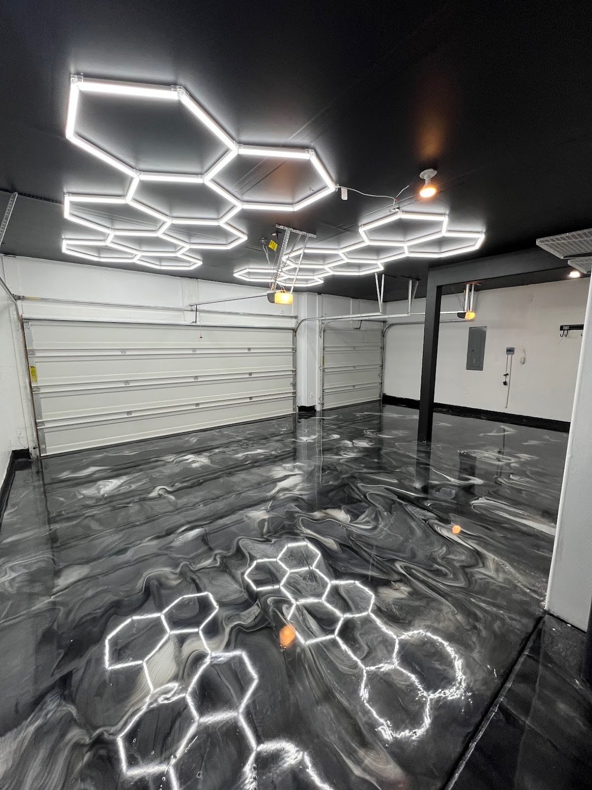 Garage interior with epoxy floor and hexagonal LED lights on ceiling, reflecting on floor.