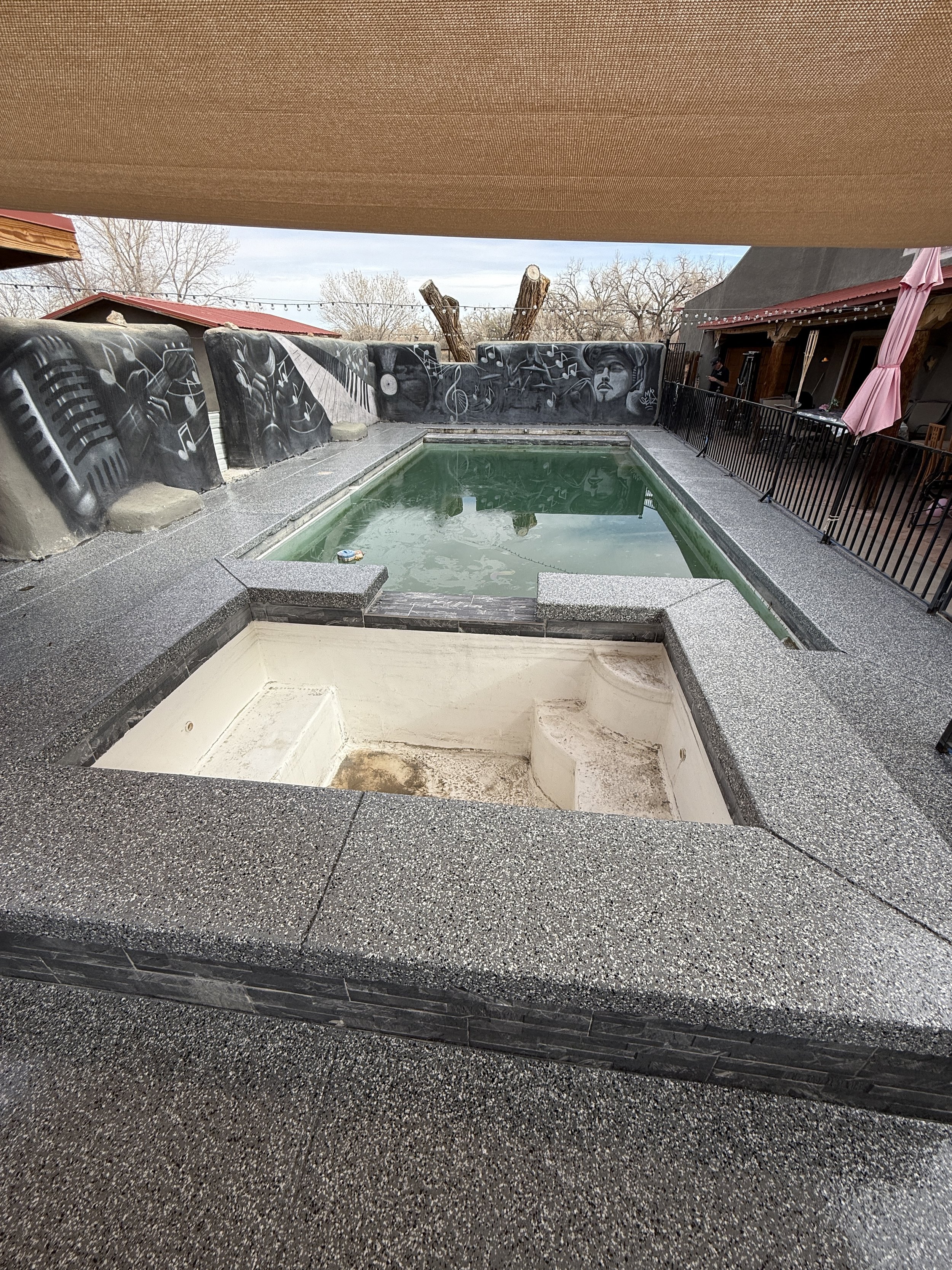 Outdoor swimming pool with murals on surrounding walls and seating area; decorative artwork features music-themed designs."}