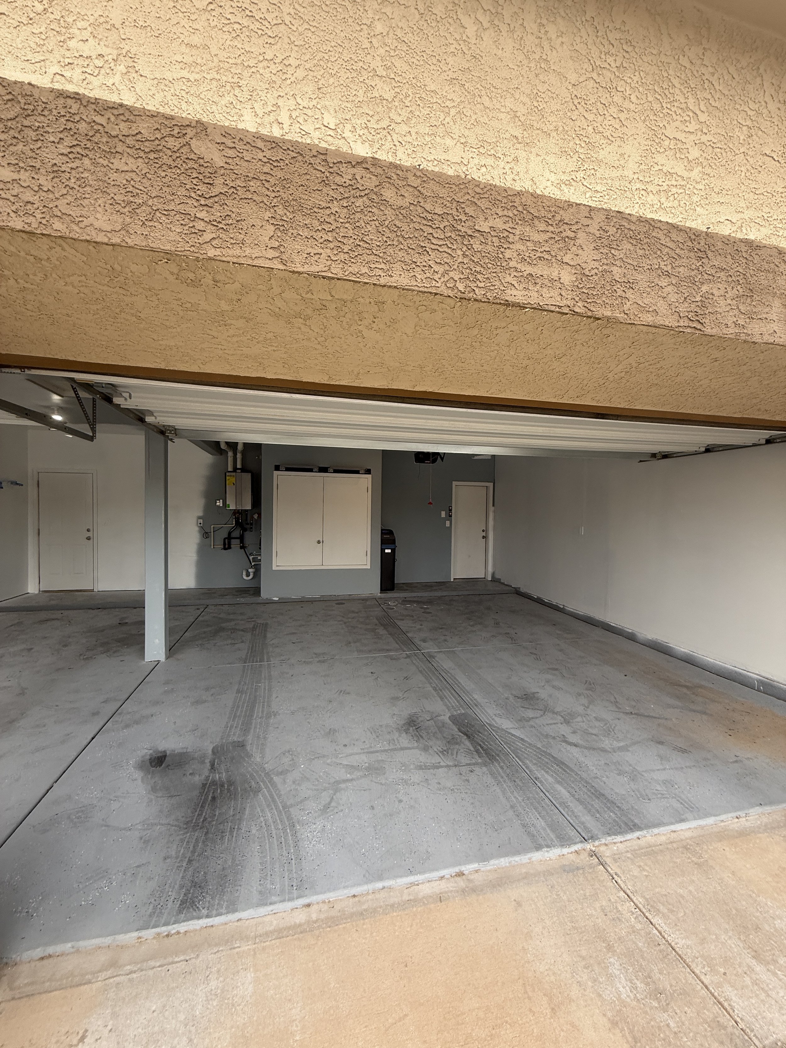 Open two-car garage with concrete floor, tire marks, and utility cabinets on the wall.