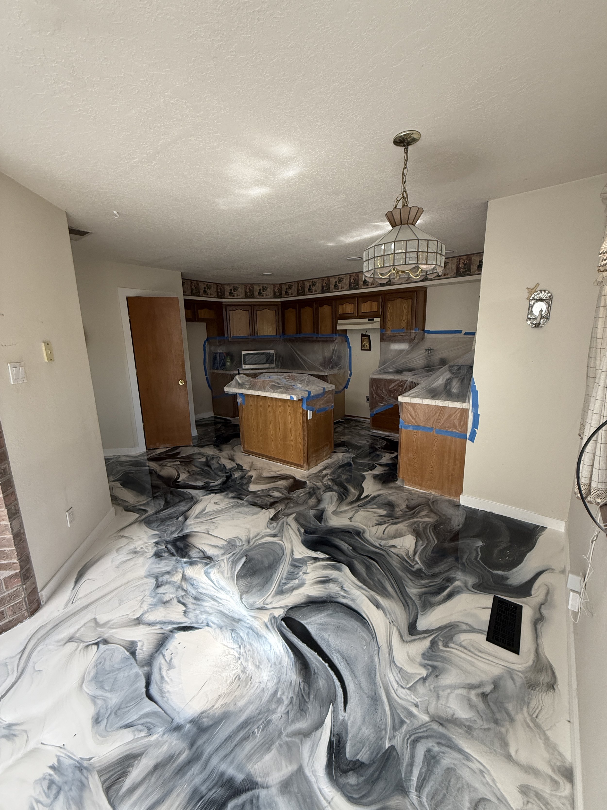 Room with a marbled epoxy floor, covered kitchen cabinets, and a pendant light.