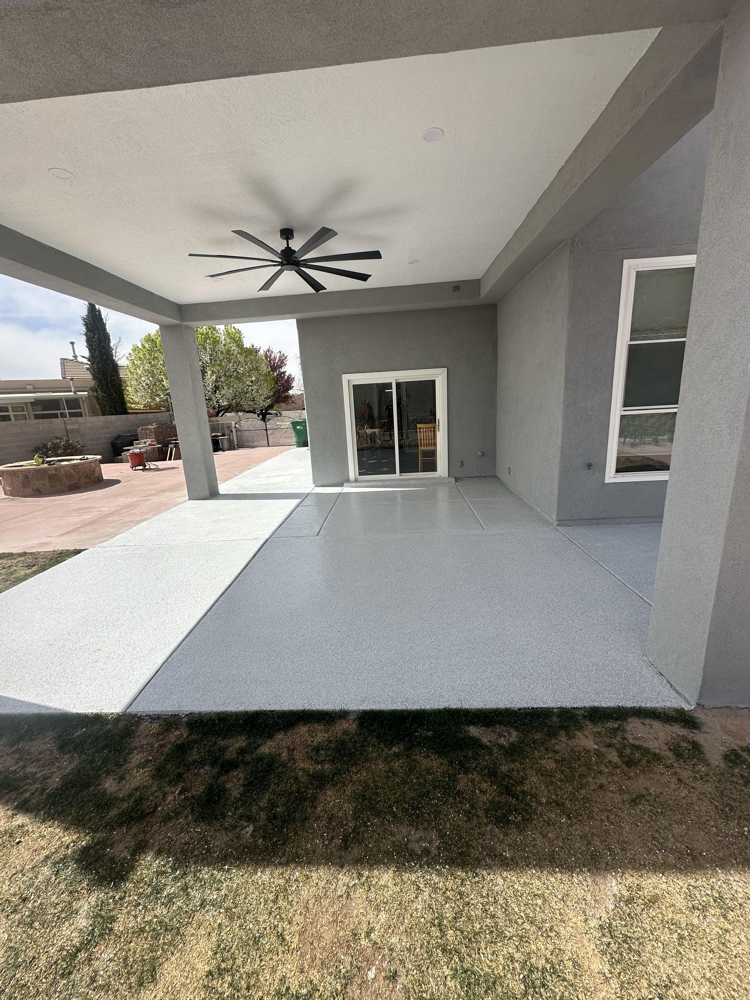 Covered patio with ceiling fan, sliding glass doors, concrete floor, adjacent grassy area.