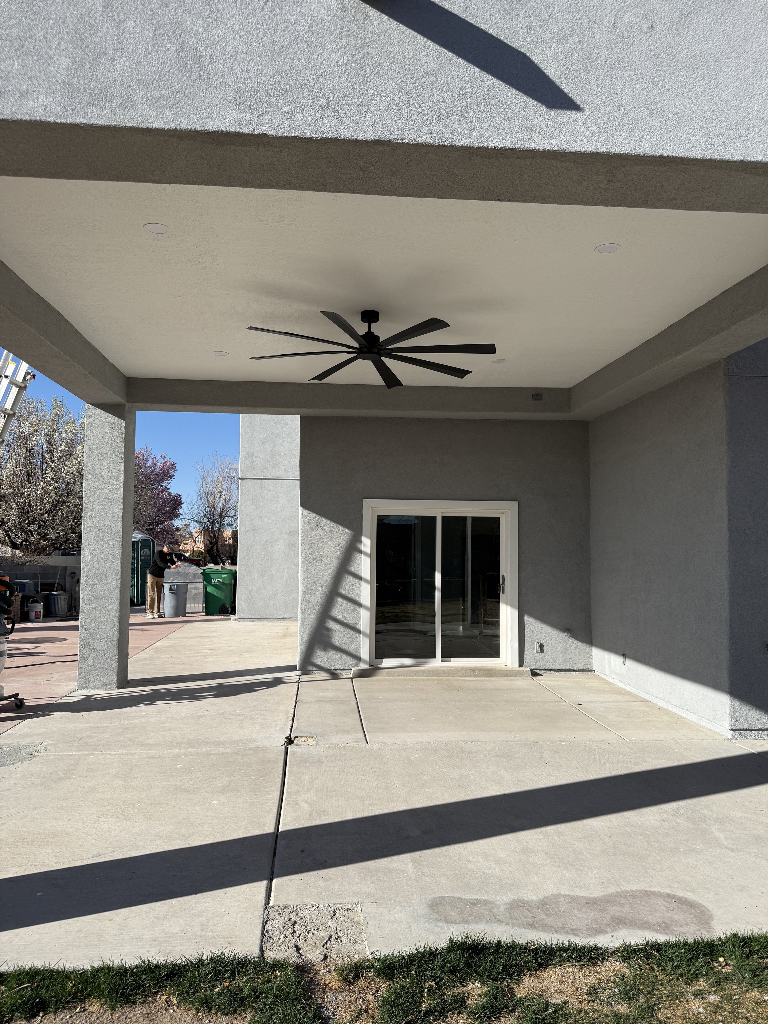 Covered patio area with a ceiling fan, sliding glass door, and concrete flooring.