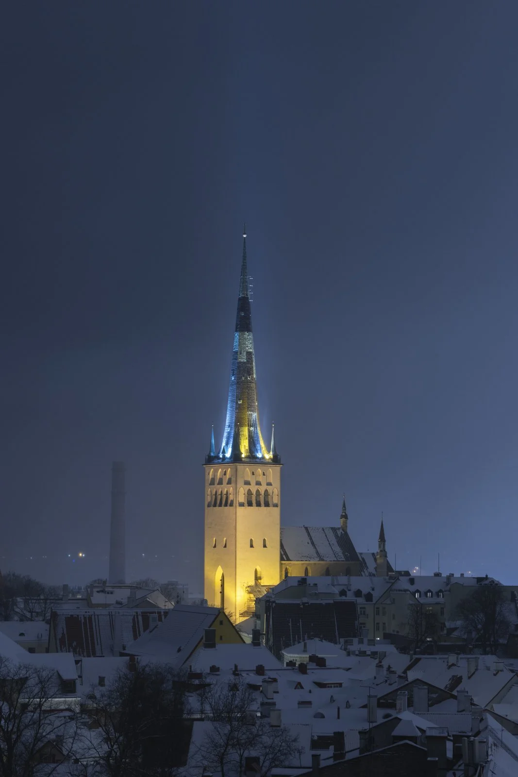 Night view of a church with a tall, illuminated steeple in snowy Tallinn, Estonia.