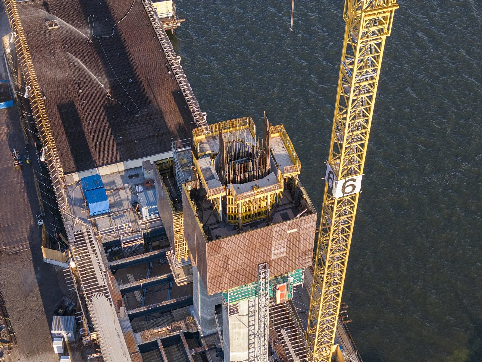 Aerial view of a construction site on water with a yellow crane, partially built structures, and equipment.