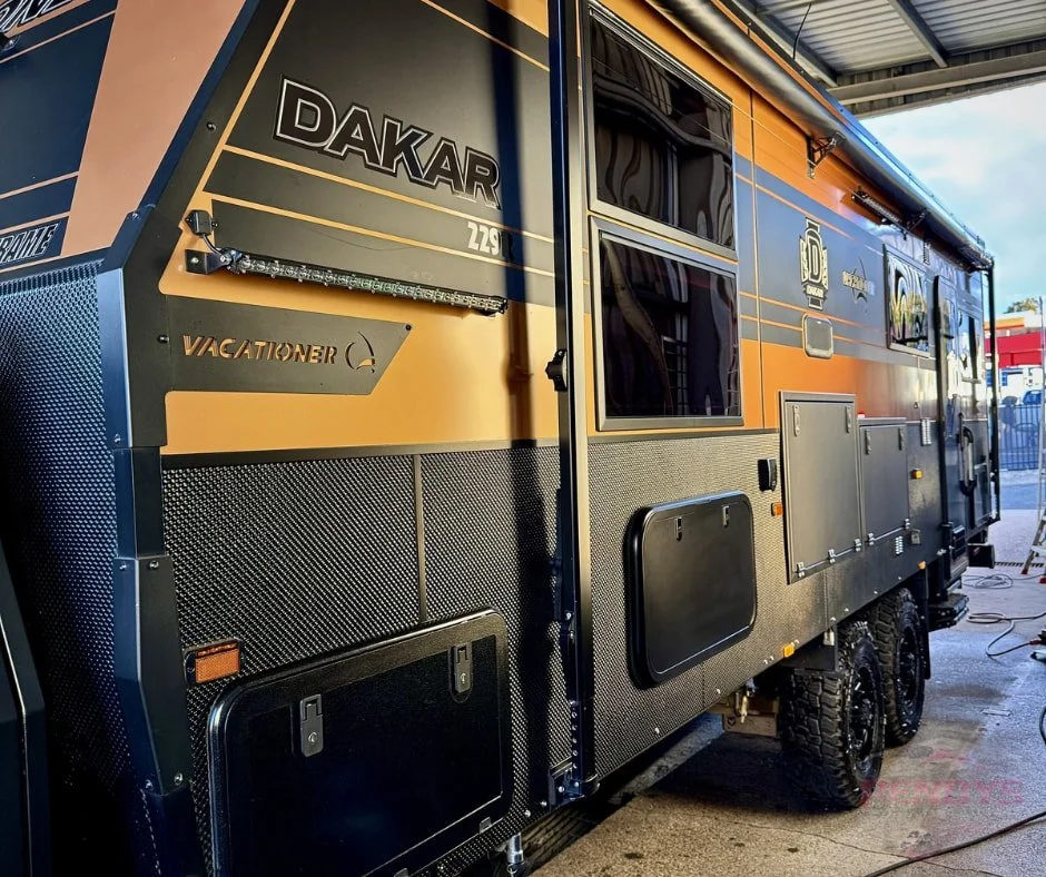 Orange and grey Dakar caravan showing its side panels, windows and storage hatches.