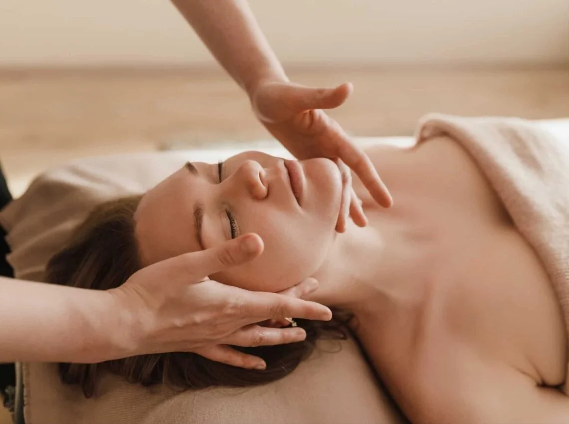 A woman receiving a facial massage in a spa setting, lying down with her eyes closed.