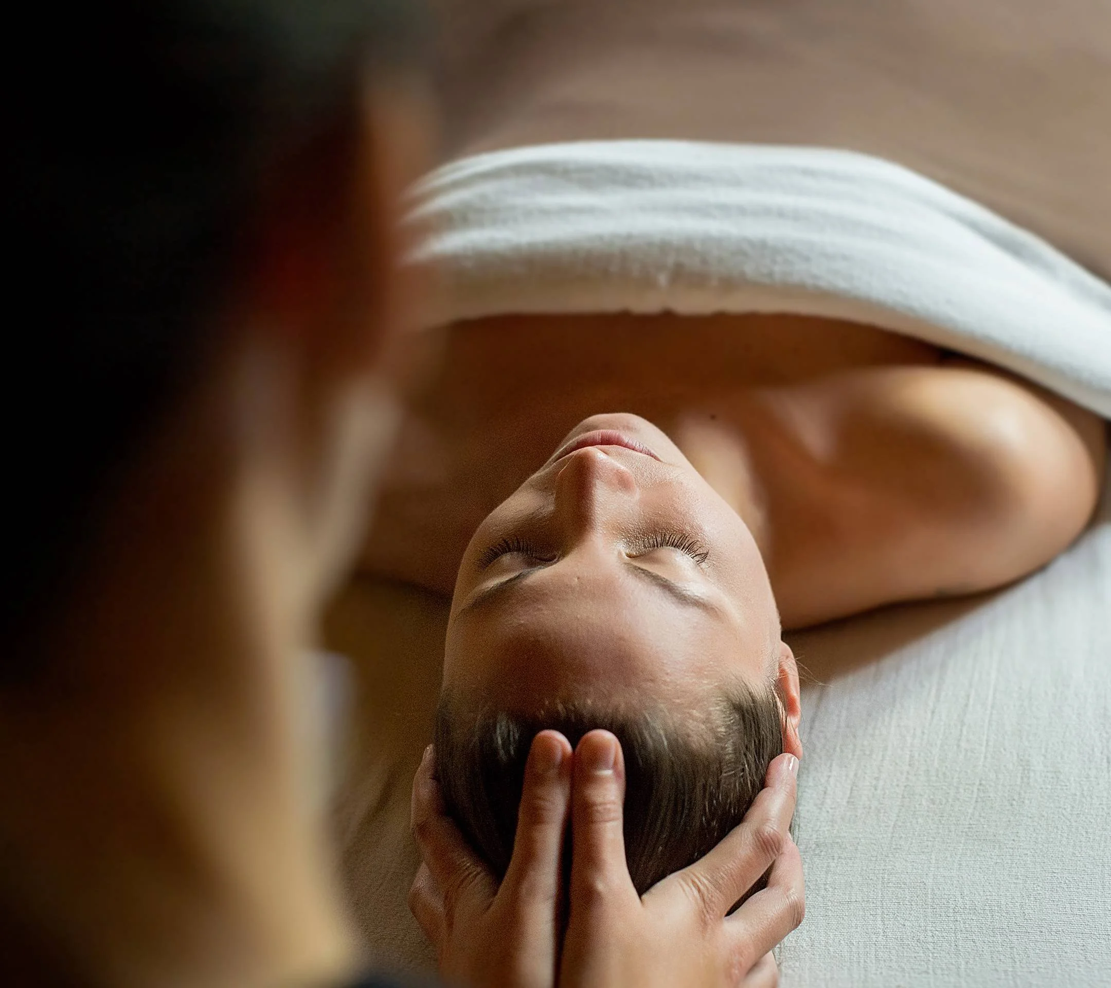 Woman receiving a massage with hands on her head, lying on her back with eyes closed.