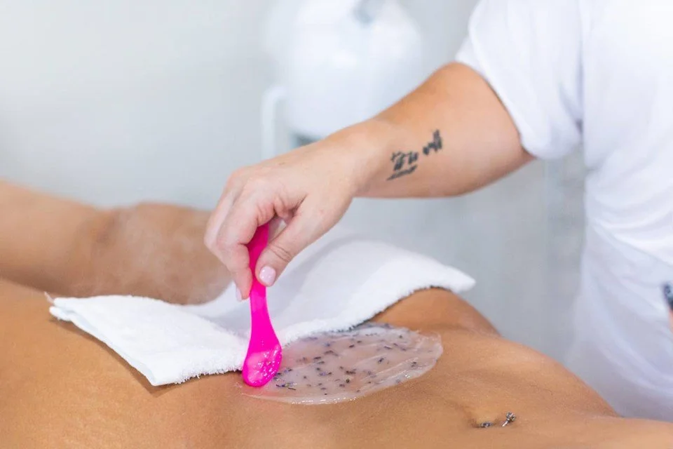 A person applying a wax strip with a pink applicator to another person's leg during a hair removal procedure.