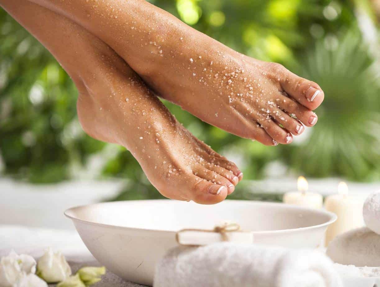 Hands sprinkling salt over a bowl during a spa or relaxation treatment with candles and towels nearby.