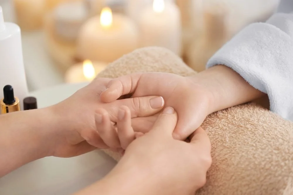 A person receiving a hand massage at a spa, with candles in the background for a relaxing atmosphere.