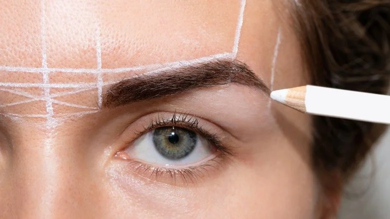Close-up of a person's eye with pre-marked lines on the forehead for cosmetic or plastic surgery, with a pencil near the eyebrow.
