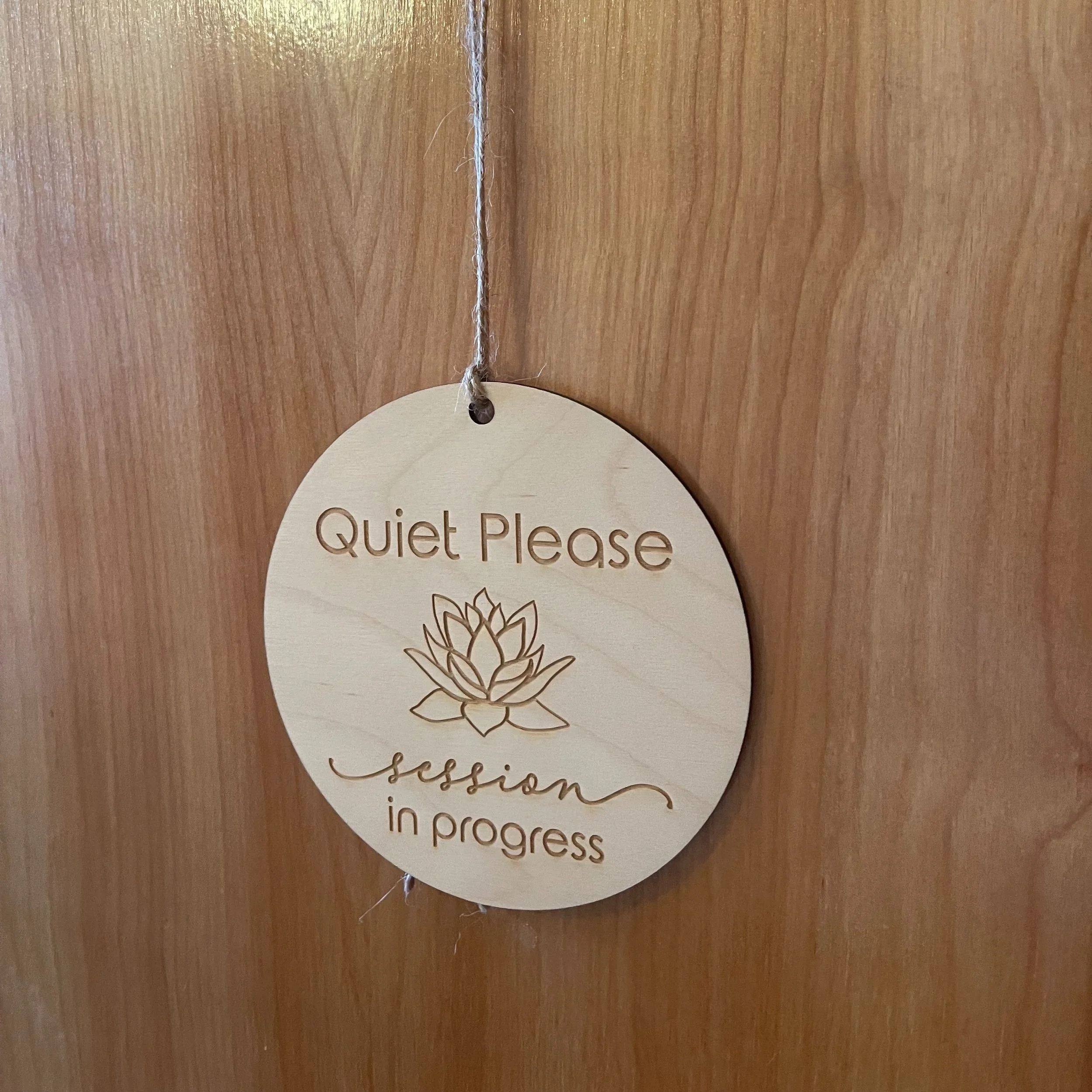 Wooden sign hanging on a door reading "Quiet Please, session in progress" with a lotus flower design.