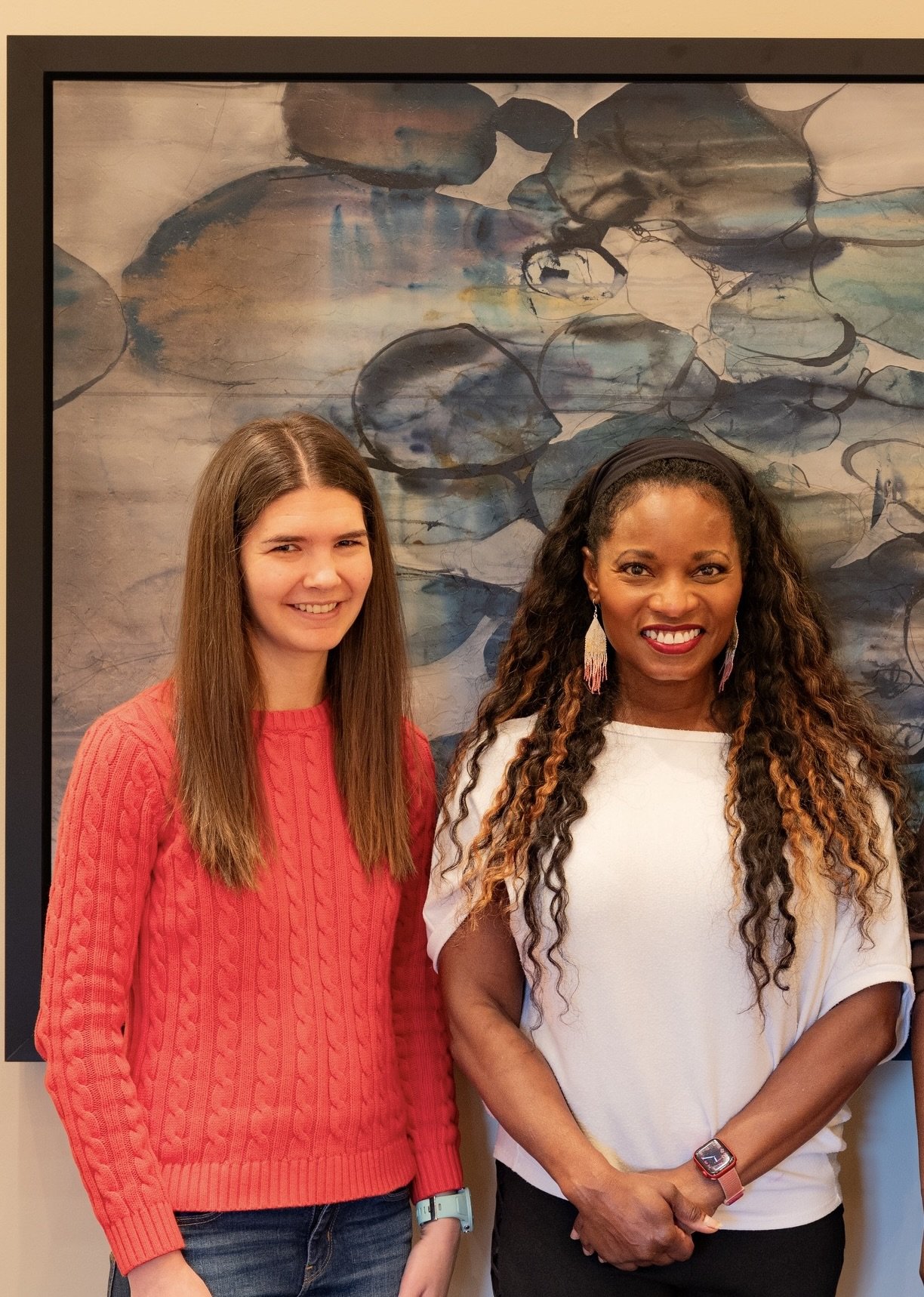 Two women standing in front of a painting of abstract water lilies, smiling at the camera.