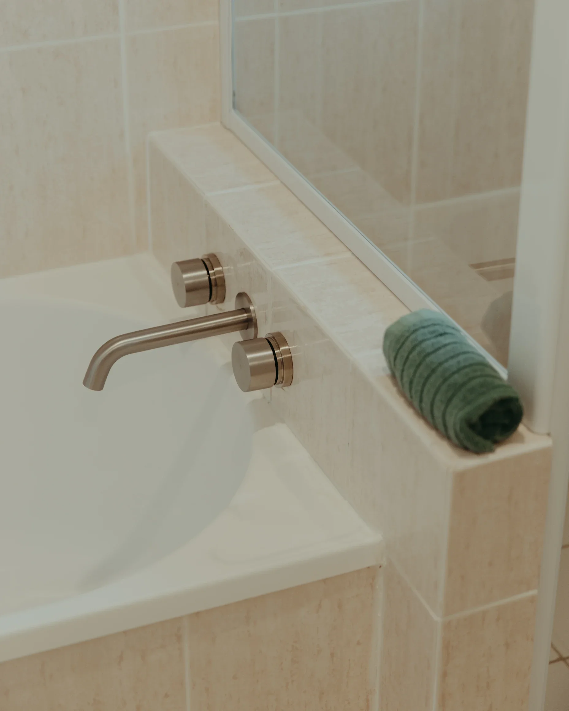 Bathroom sink with a brushed nickel faucet and knobs, with a rolled green towel on the counter.