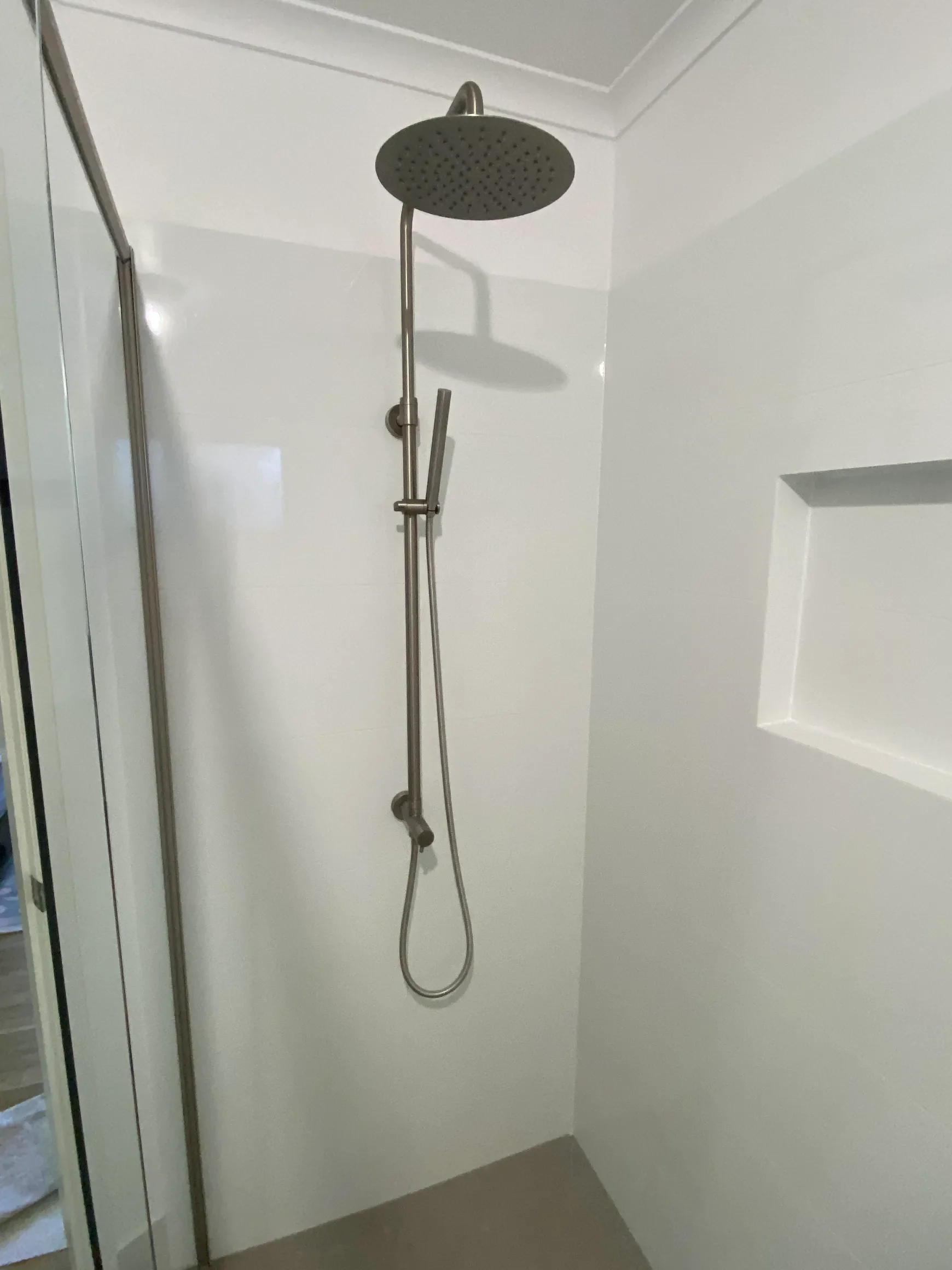 A walk-in shower with a round rainfall showerhead mounted from the ceiling and a handheld showerhead attached to a vertical bar on the wall inside a tiled bathroom.