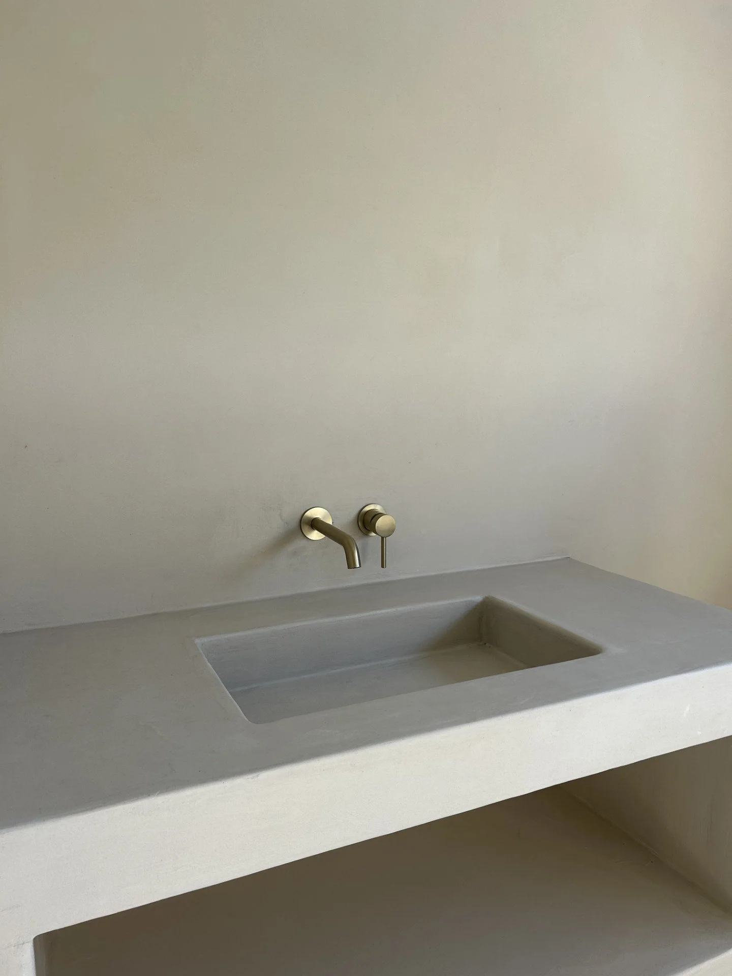 A minimalist concrete countertop with an integrated rectangular sink and a wall-mounted faucet with a handle, set against a plain, light-colored wall.